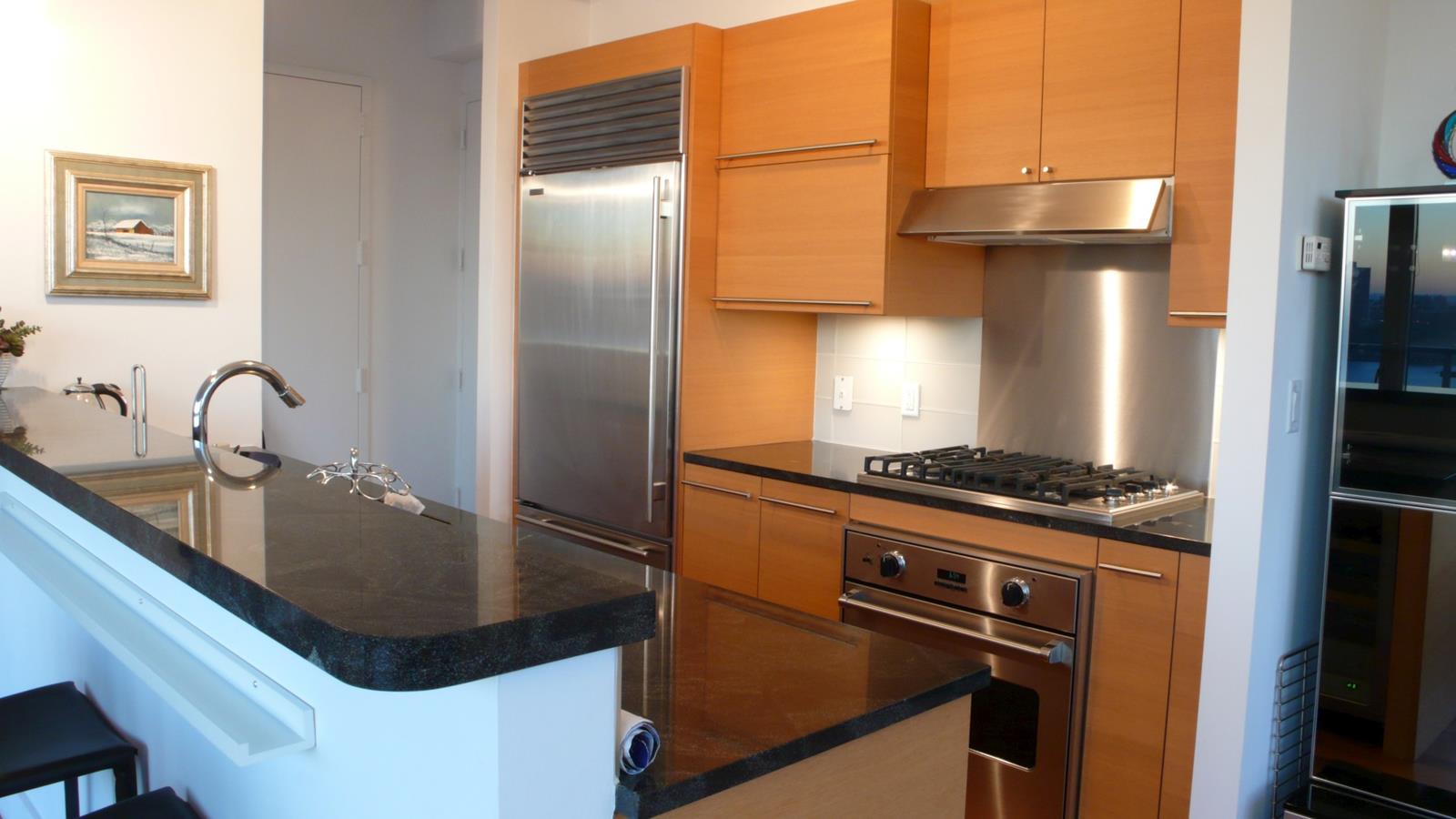 Kitchen with warm wood cabinets, stainless-steel appliances, and a dark stone breakfast bar.