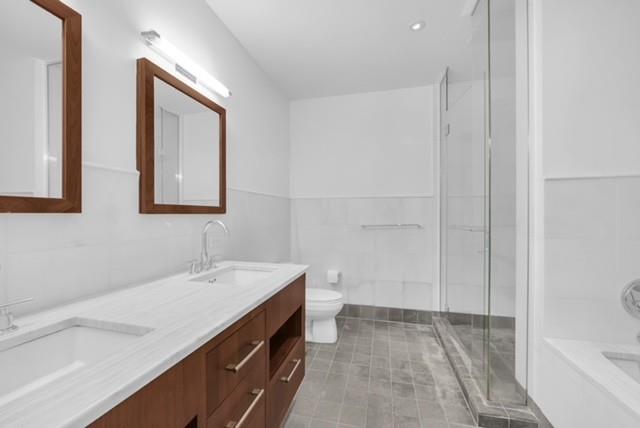 Modern bathroom with a long wood vanity, gray tile floor, glass shower, and bathtub.