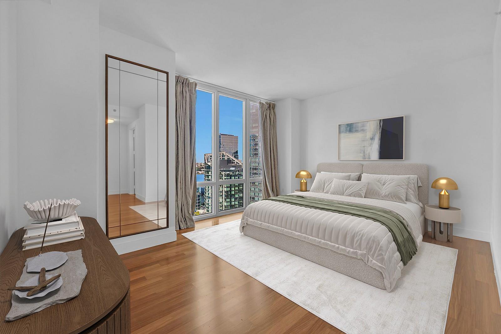 Staged bedroom with a king-size bed, mirrored wardrobe, and floor-to-ceiling windows overlooking water and buildings.