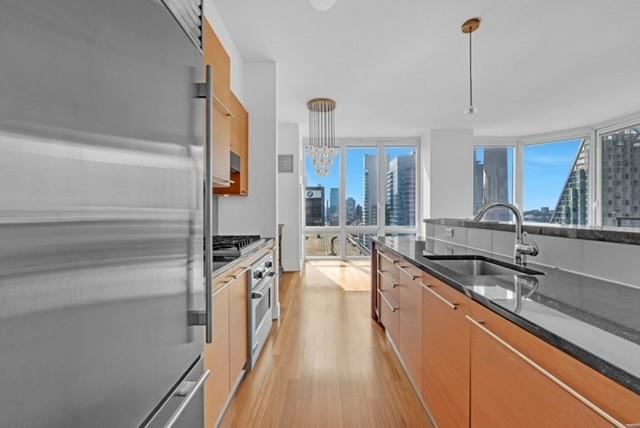Modern apartment kitchen with wood cabinetry, a long island, and city views through large windows.