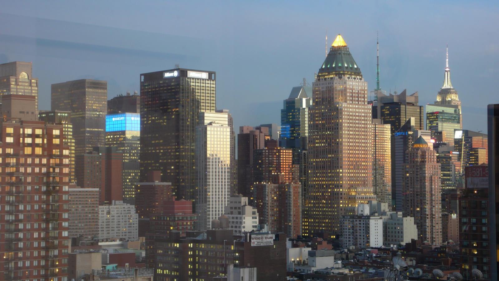 New York City skyline at dusk, with the Empire State Building and illuminated gold-capped tower.