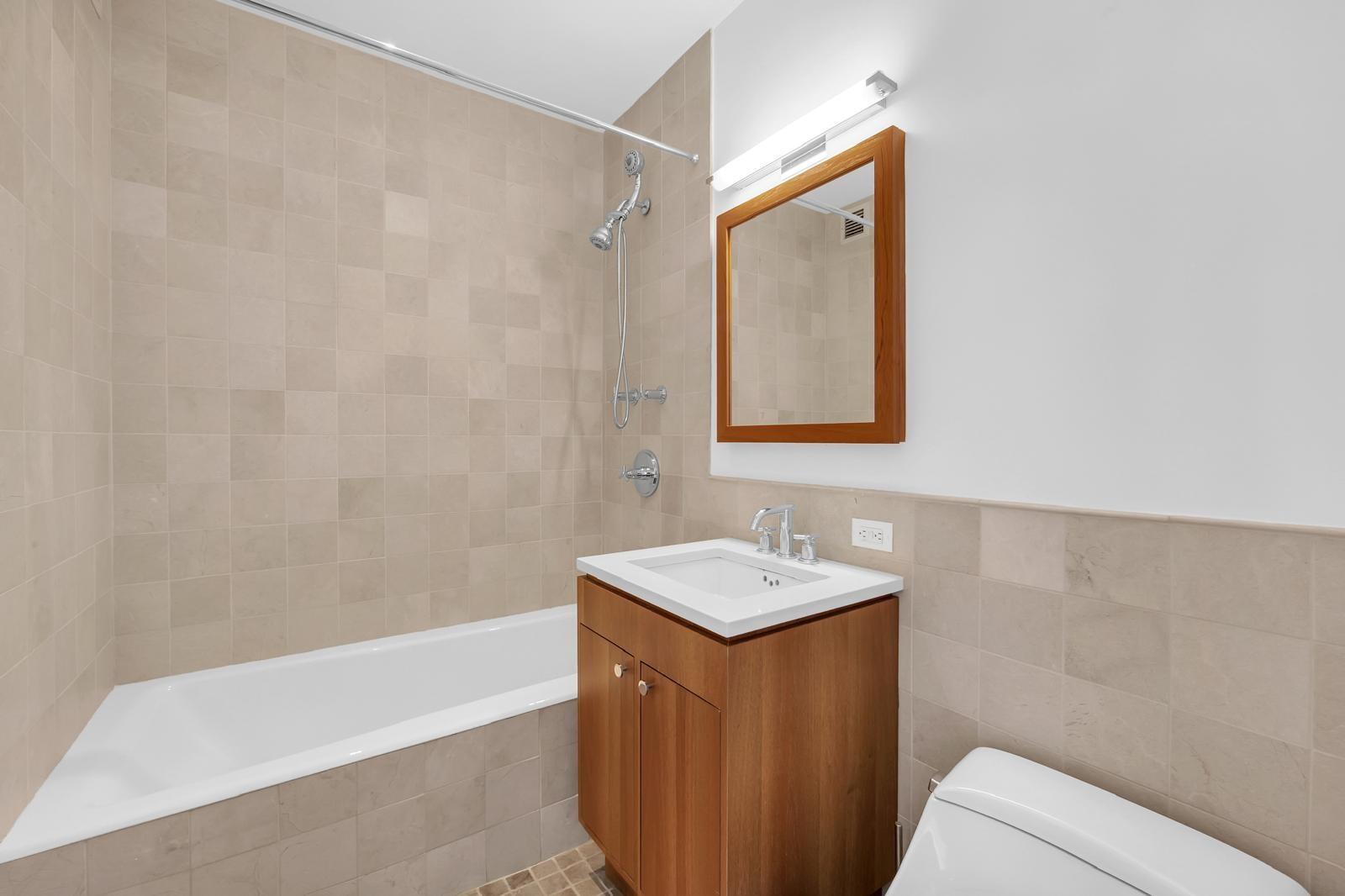Bathroom with beige tile, a built-in bathtub, and a wood vanity with framed mirror.