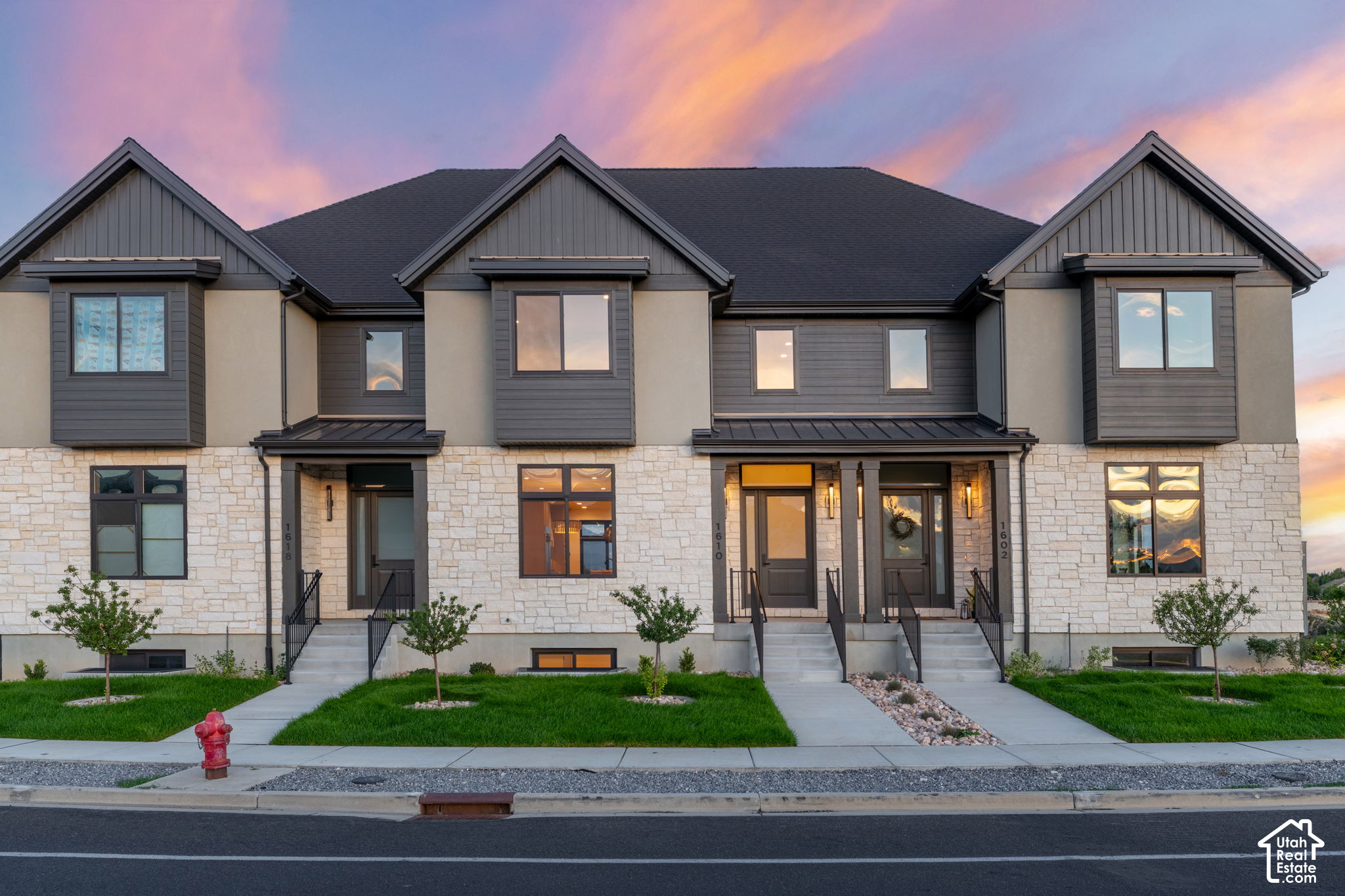 Two attached modern homes with stone facades and peaked gables beneath a colorful dusk sky.