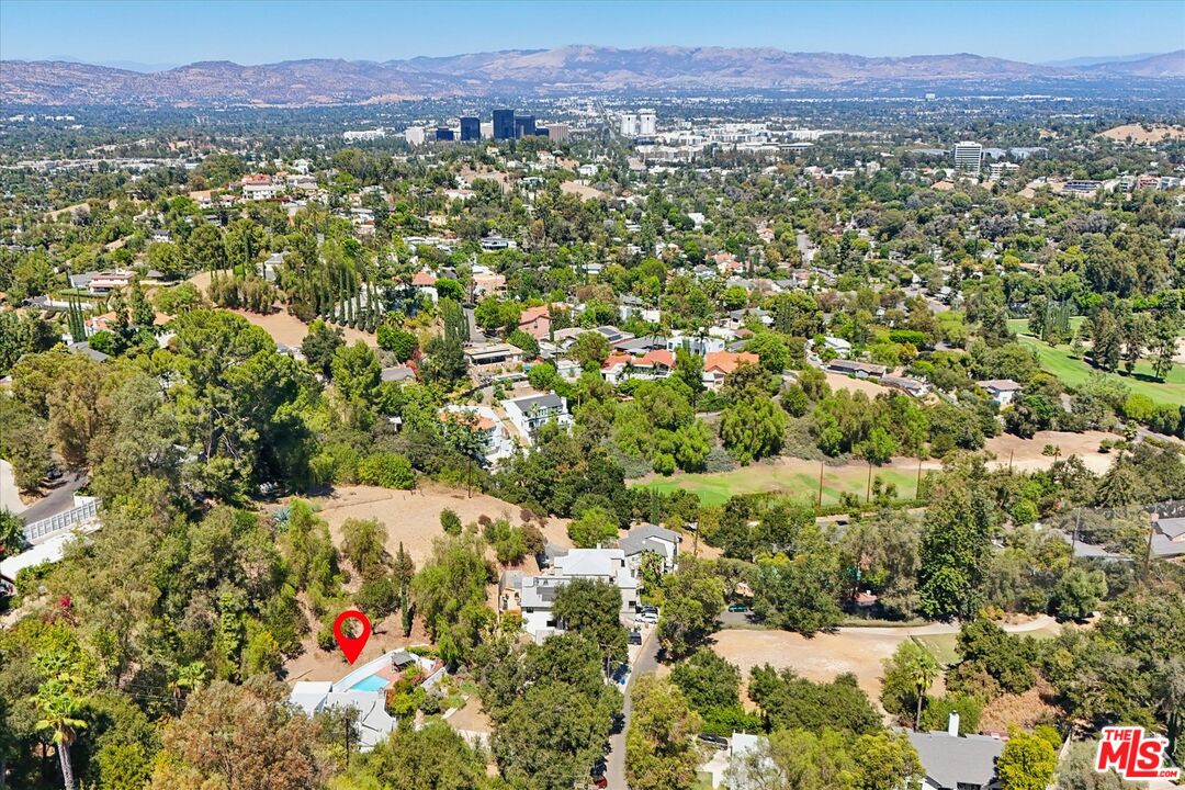 Aerial view of a hillside neighborhood with the marked home, city skyline, and distant mountains.