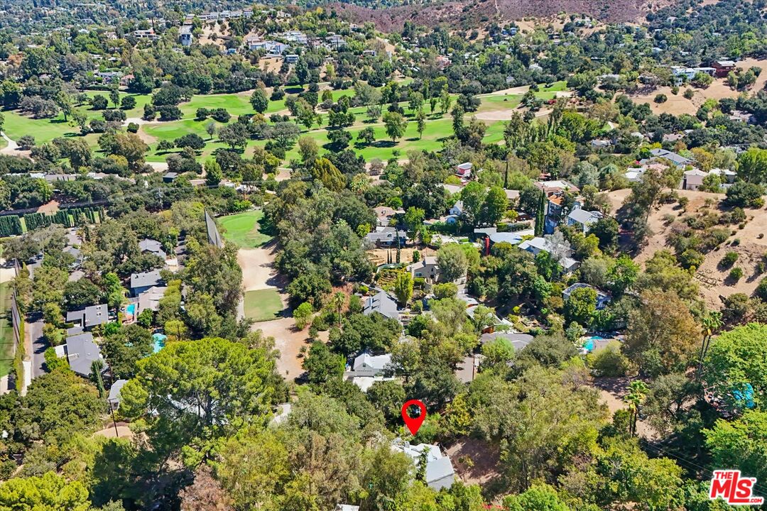 Aerial view of the marked property among wooded hillside homes near a green golf course.