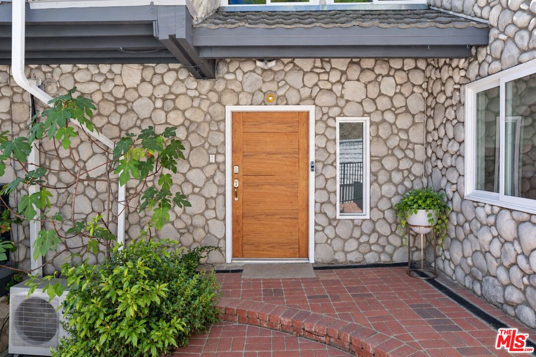 Home entrance with a wood door set in a stone facade and a curved brick patio.