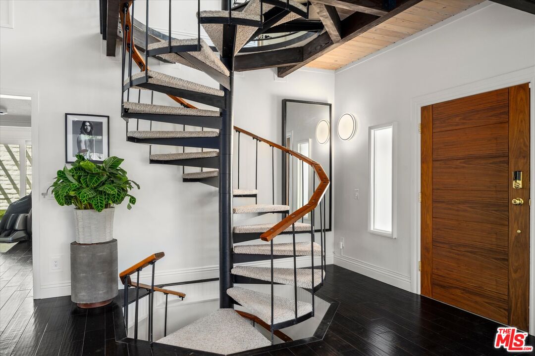 Entryway with a curved carpeted staircase, wood handrail, dark floors, and a wooden front door.