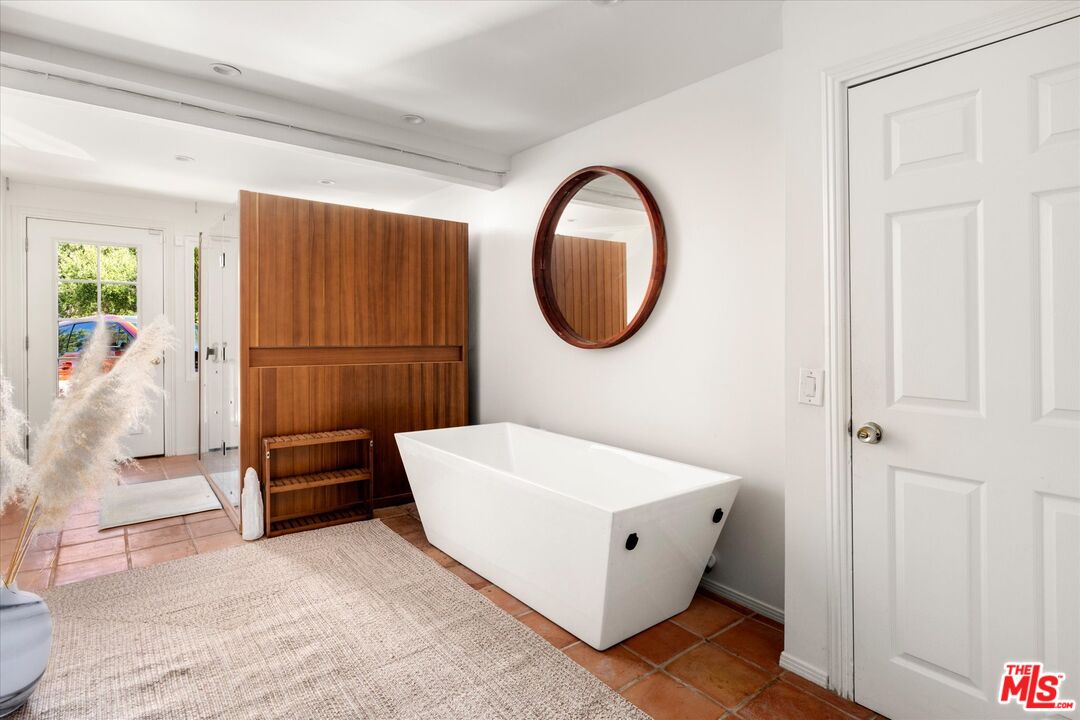 Bathroom with a freestanding white tub, terracotta tile, and a tall walnut-toned cabinet.