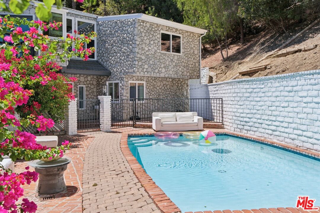 Backyard pool beside a stone-clad home, with patio seating and bright bougainvillea.