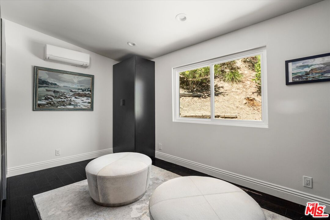 Sitting room with two round ottomans, dark tile flooring, and a window overlooking a hillside.
