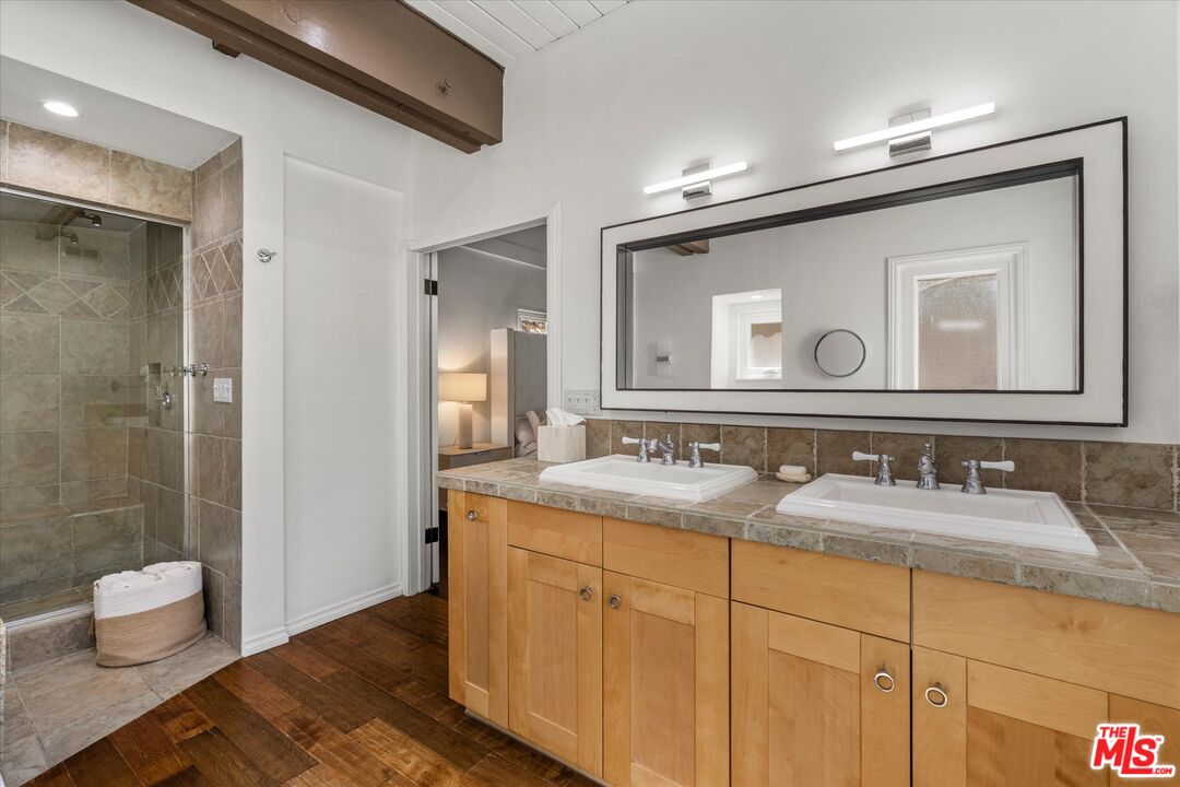 Bathroom with a wood double vanity, large framed mirror, and tiled walk-in shower.