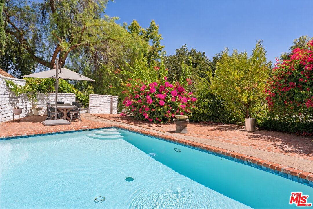 Swimming pool with broad entry steps, brick patio dining area, and flowering bougainvillea.