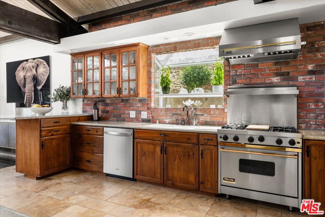 Kitchen with wood cabinetry, exposed brick, and a stainless steel Viking range beneath a large hood.
