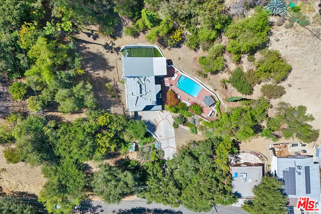 Aerial view of a tree-surrounded home with a bright blue swimming pool and paved driveway.