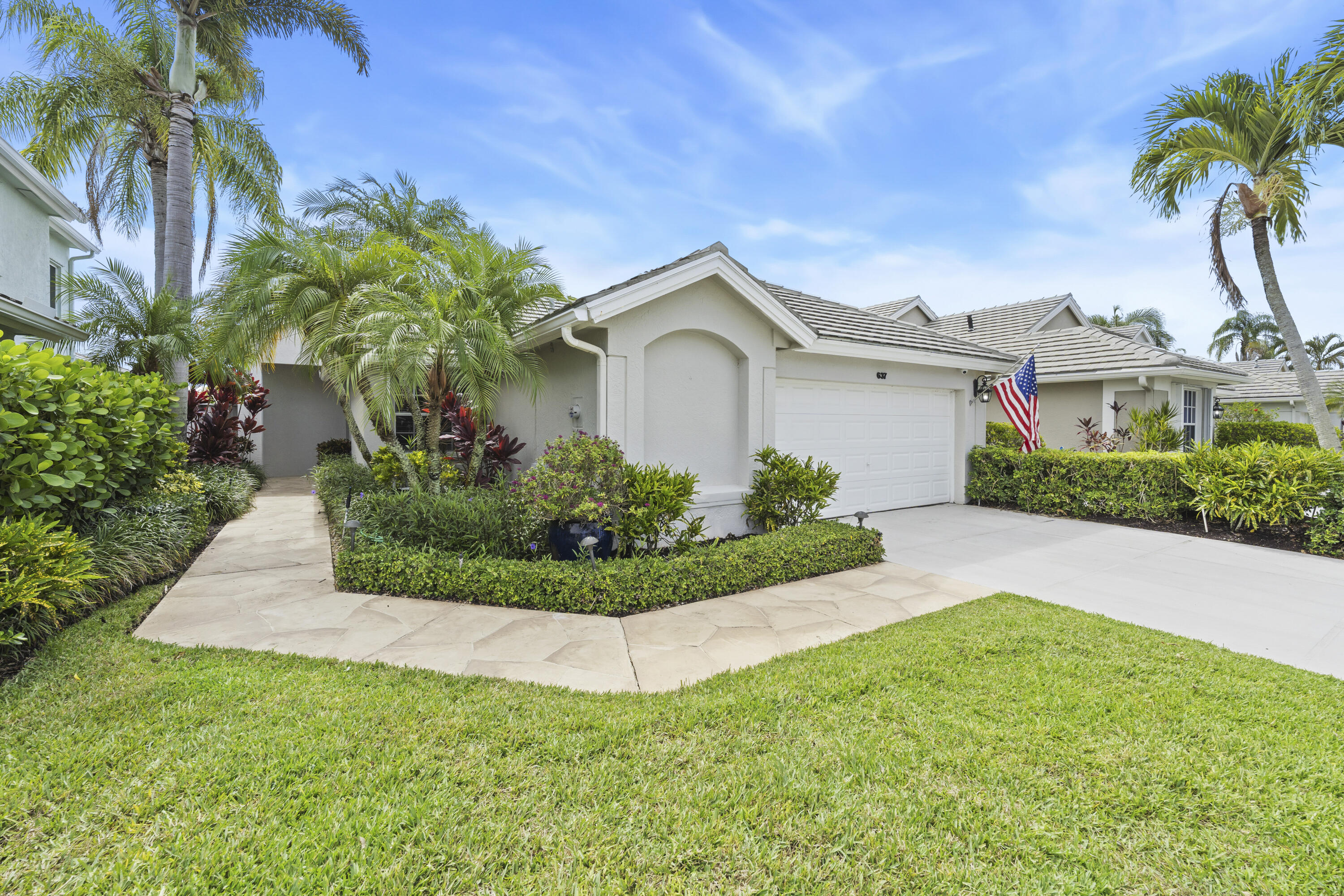 Home at 637 Masters Way with a white garage, tropical landscaping, and an American flag.