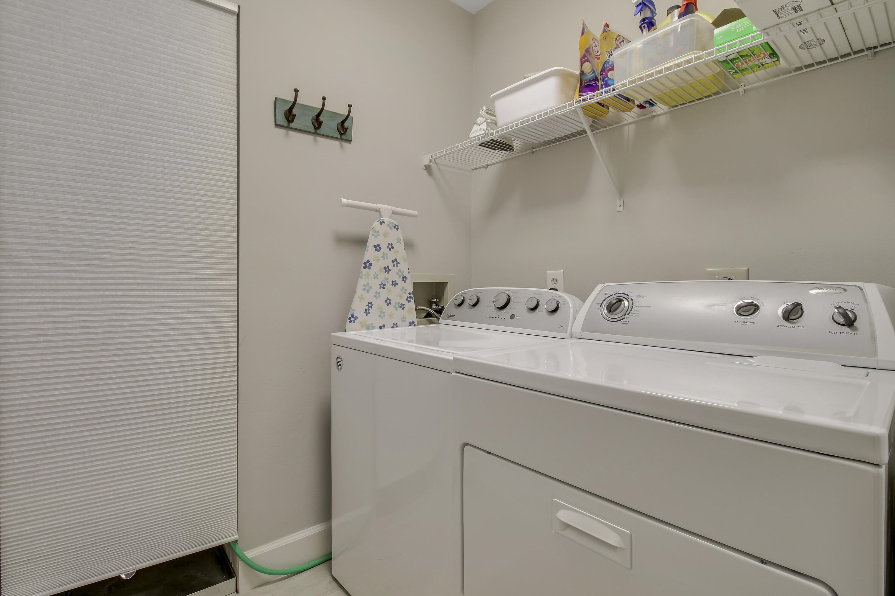 Laundry room with white washer and dryer beneath wire shelving stocked with supplies.