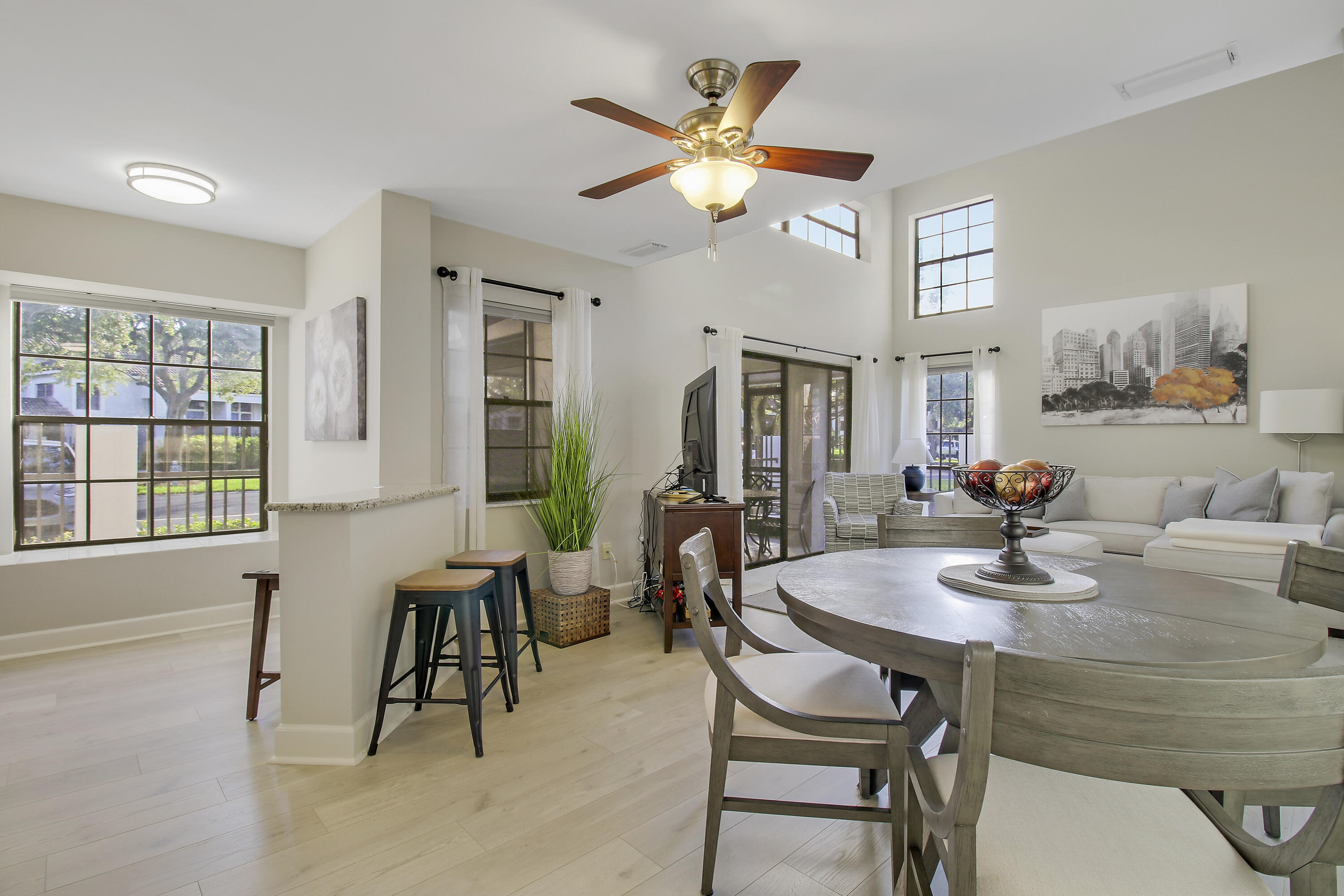 Open-plan living and dining room with a round table, pale sectional, and tall windows.