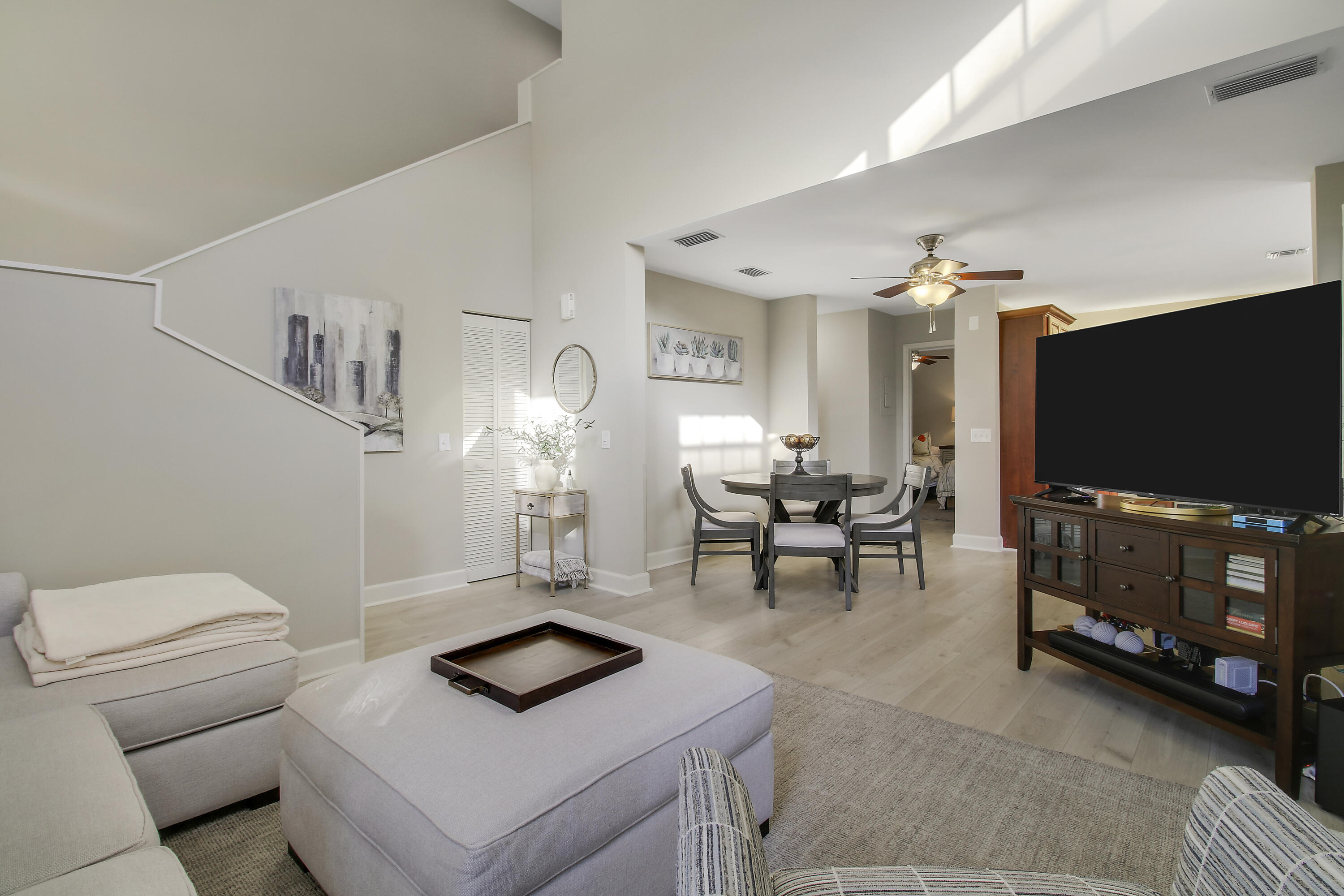Furnished living room opening to a dining area, with a high ceiling and staircase.