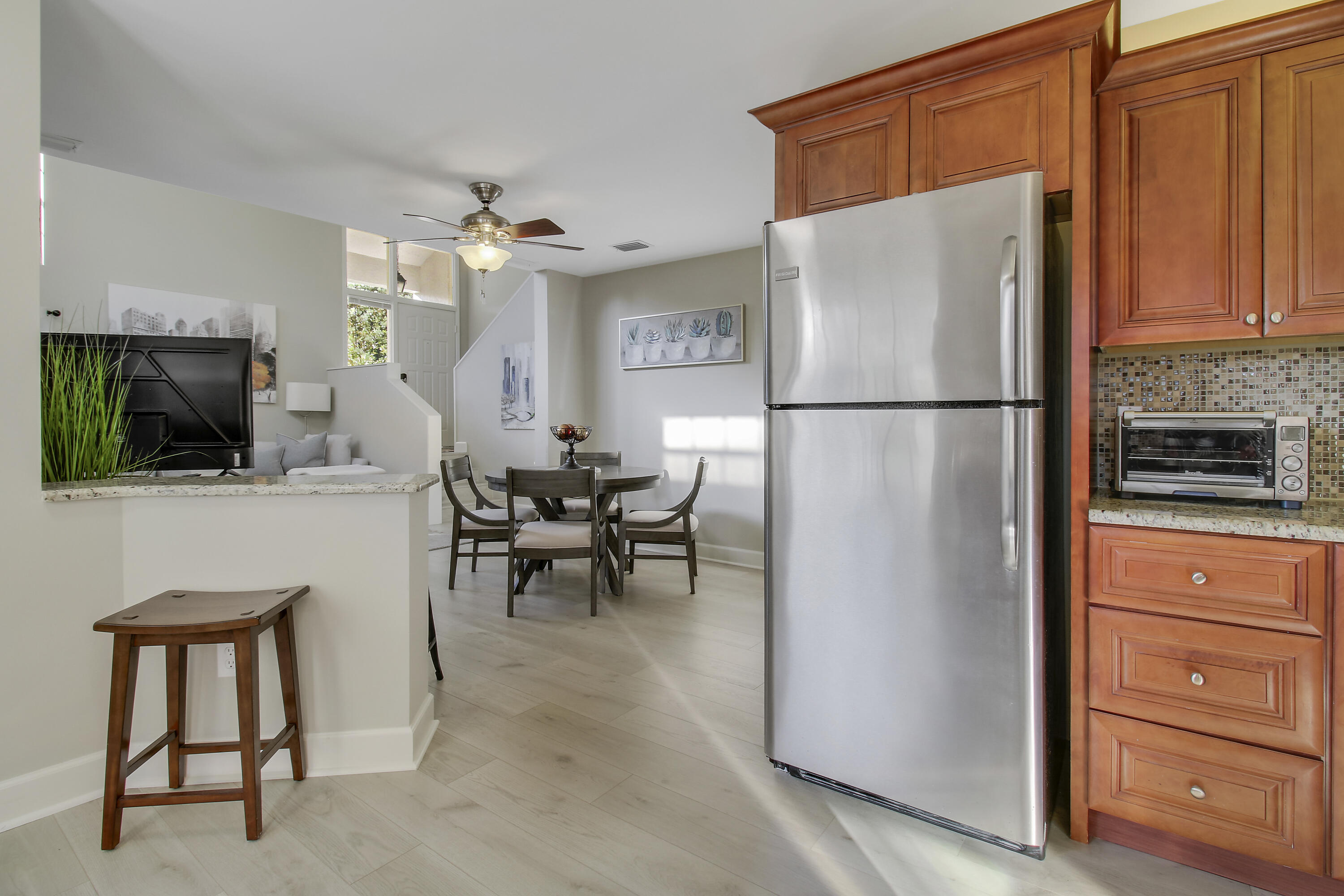 Open-plan kitchen with wood cabinets and stainless refrigerator beside a furnished dining area.
