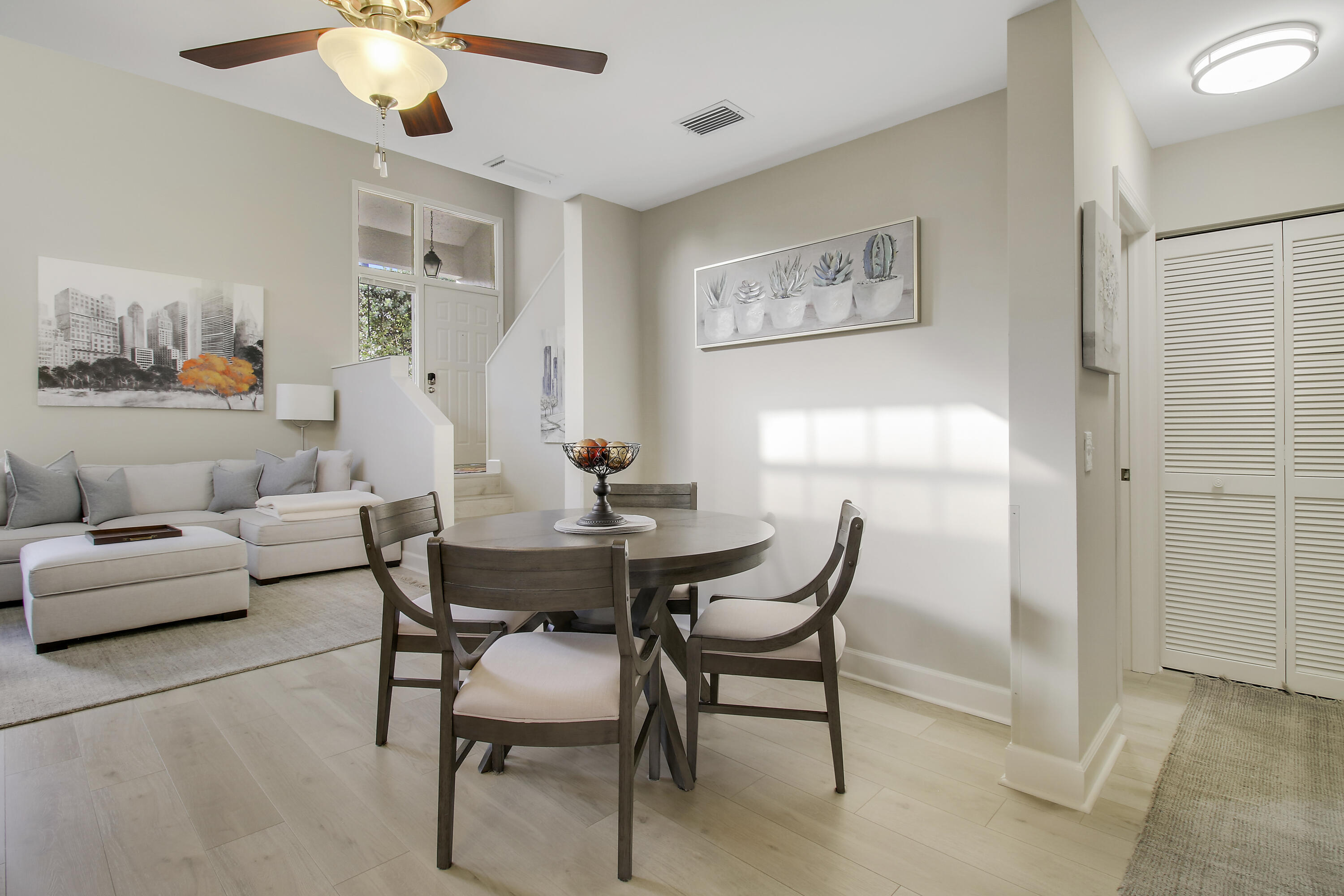 Dining area with a round wood table beside a light sectional and entry stairs.