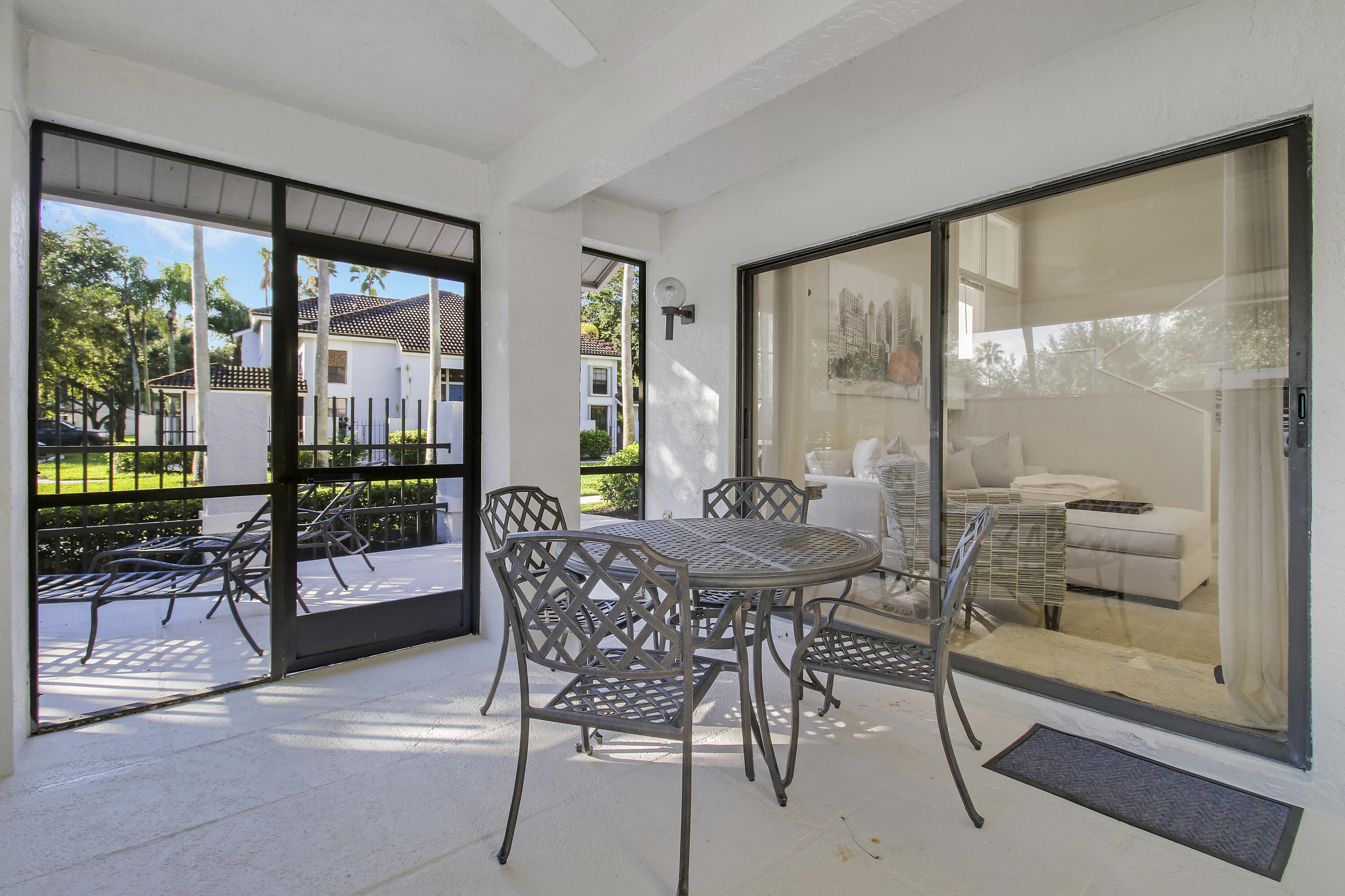Covered patio with metal dining set beside sliding doors overlooking lounge chairs and landscaped grounds.