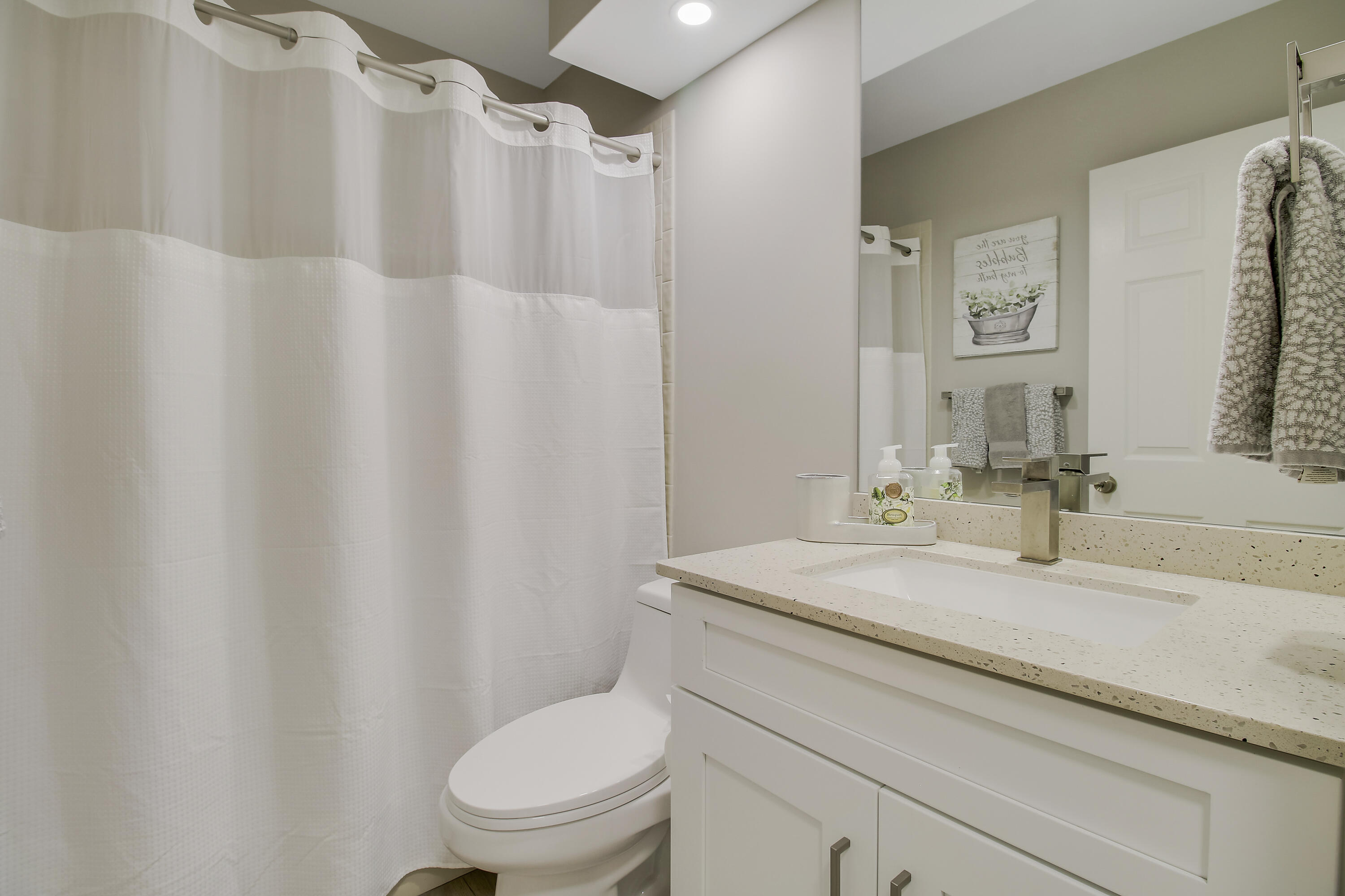 Bathroom with a white shower curtain, toilet, and vanity with a speckled countertop.