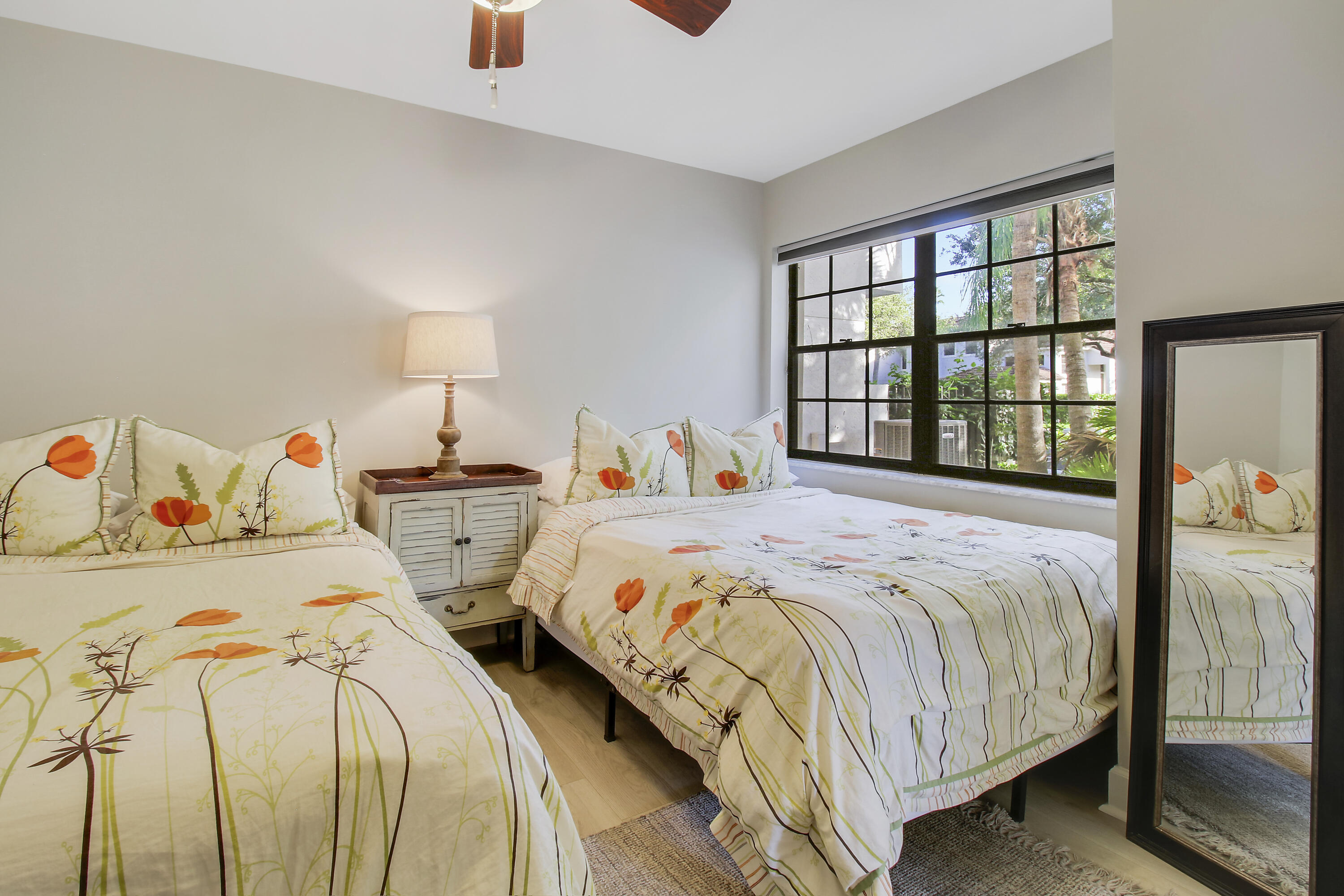 Bedroom with two floral-covered beds, a large window, and a full-length mirror.