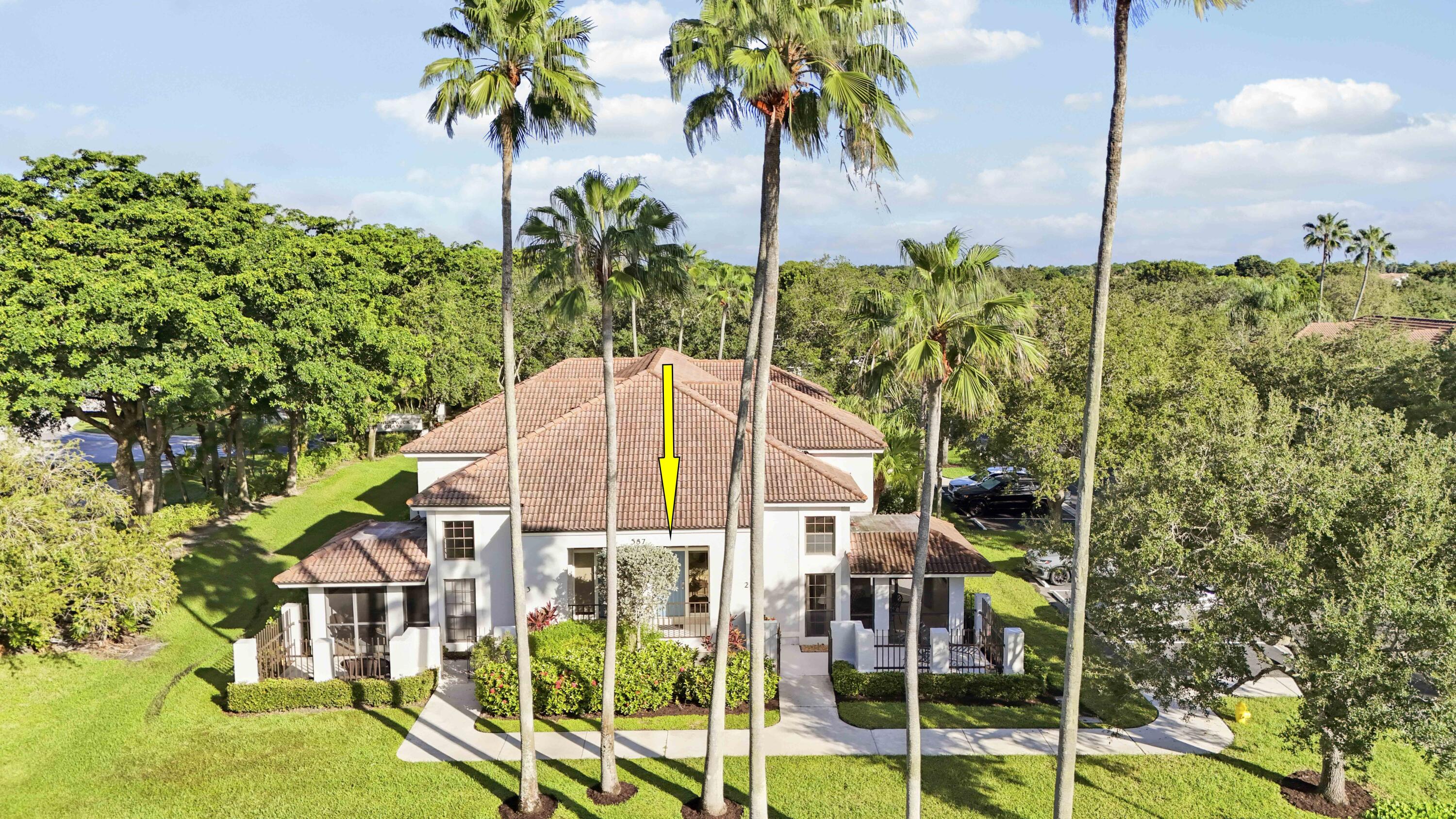 Front of a white, tile-roofed home framed by tall palms, with a yellow arrow marking the entrance.