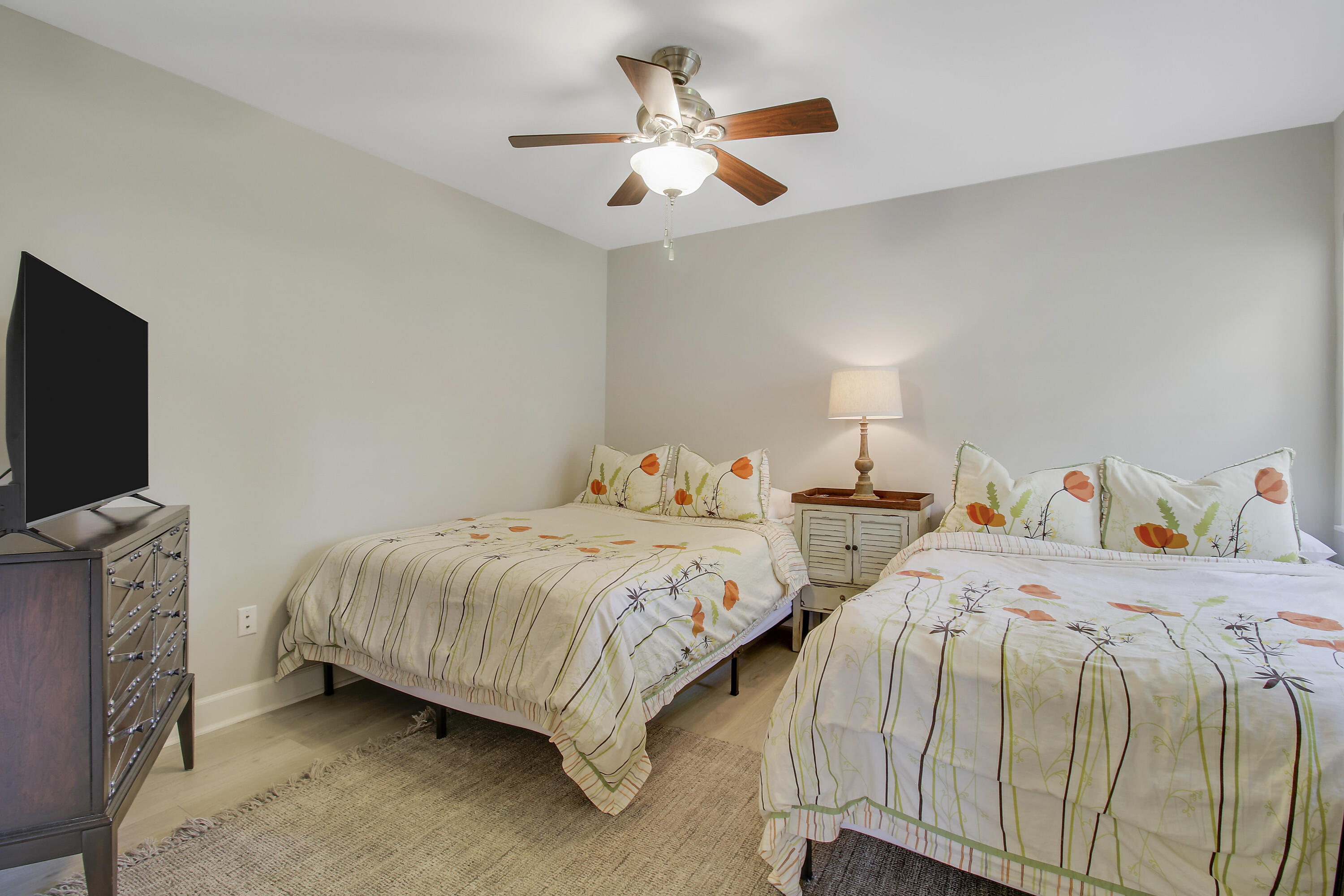 Bedroom with two floral-bedding beds, a shared nightstand, ceiling fan, and television.