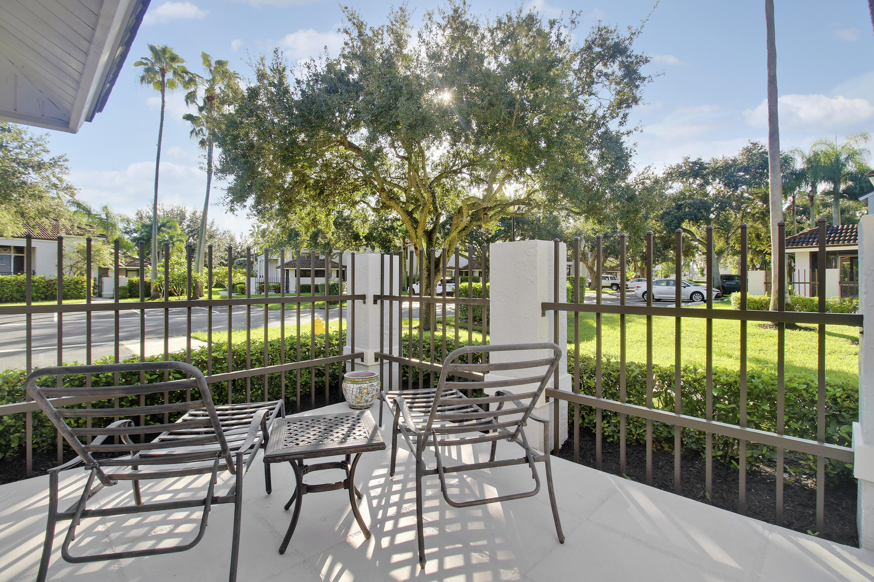 Fenced patio with metal seating overlooking landscaped grounds and a large shade tree.