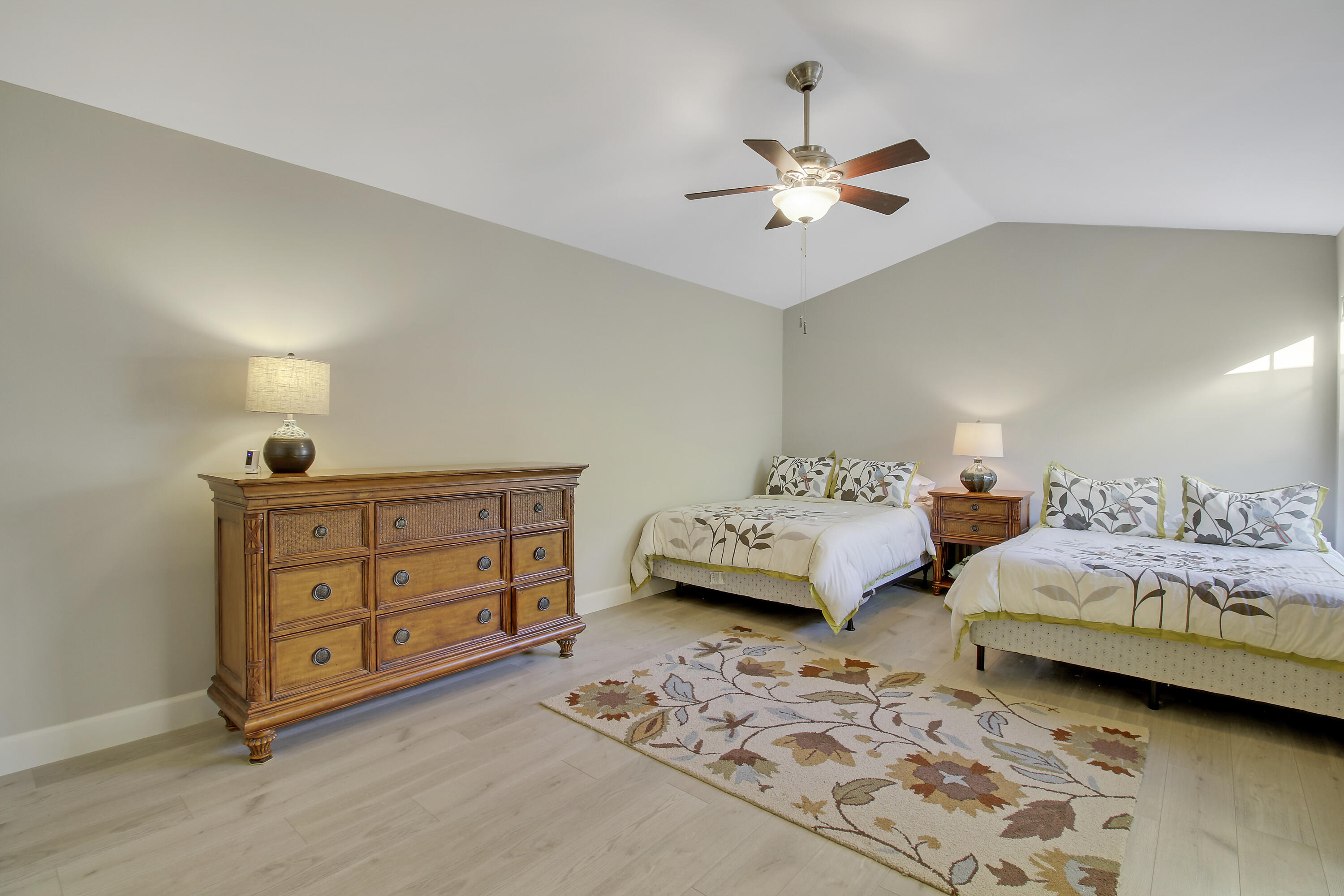 Bedroom with two beds, patterned bedding, a wooden dresser, and a floral rug.