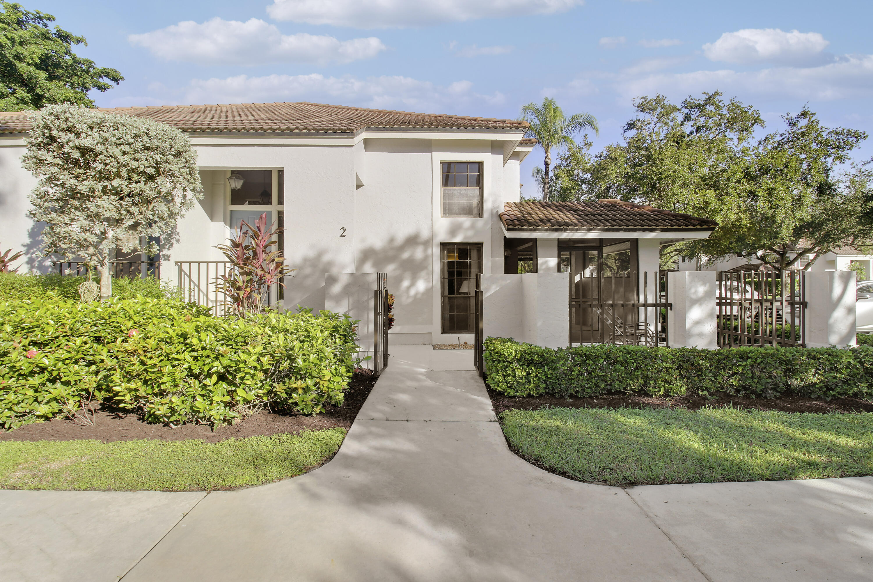 Two-story residence with a tile roof, landscaped entry walkway, and gated covered patio.