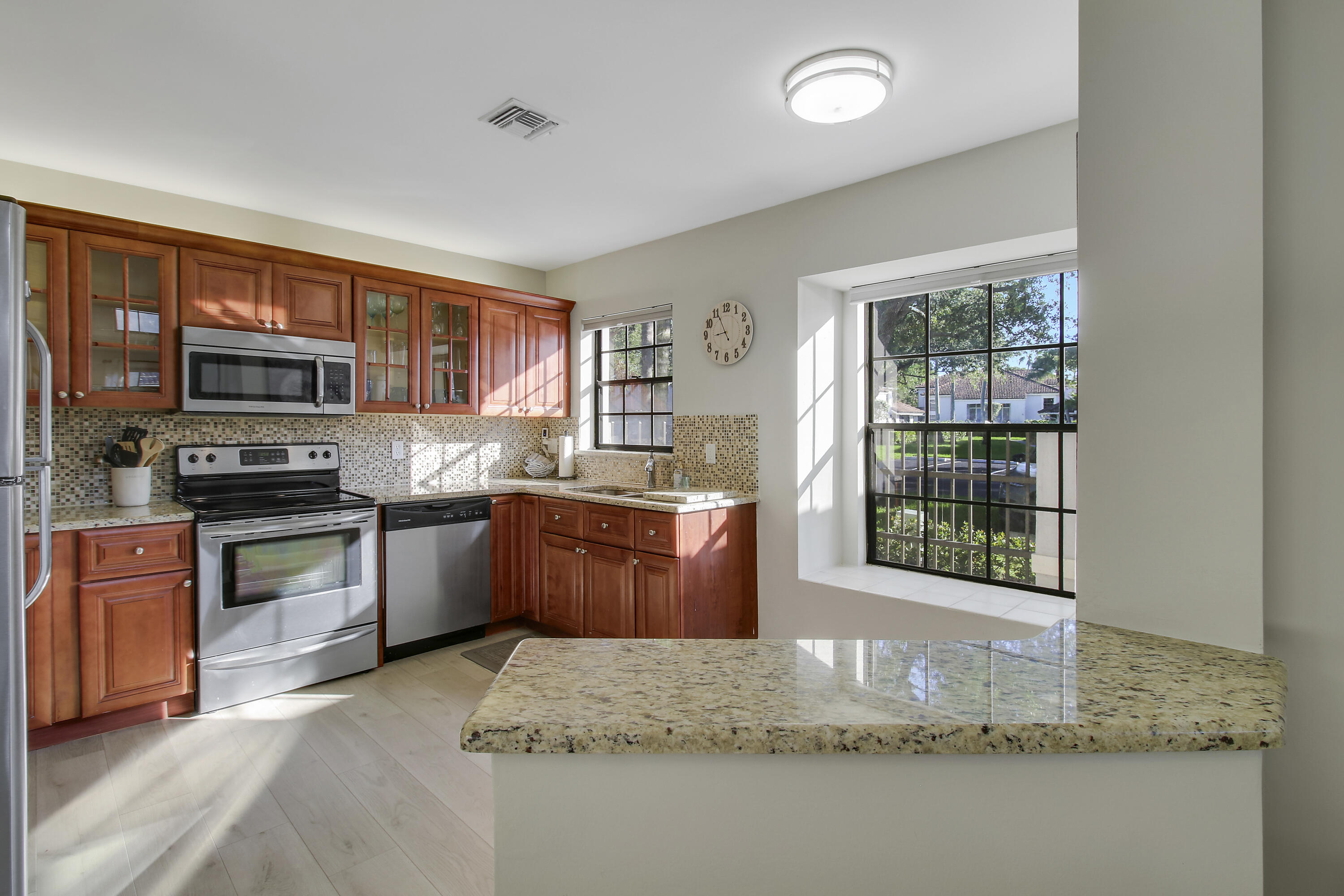 Kitchen with reddish wood cabinets, stainless steel appliances, and a granite island beside sunlit windows.