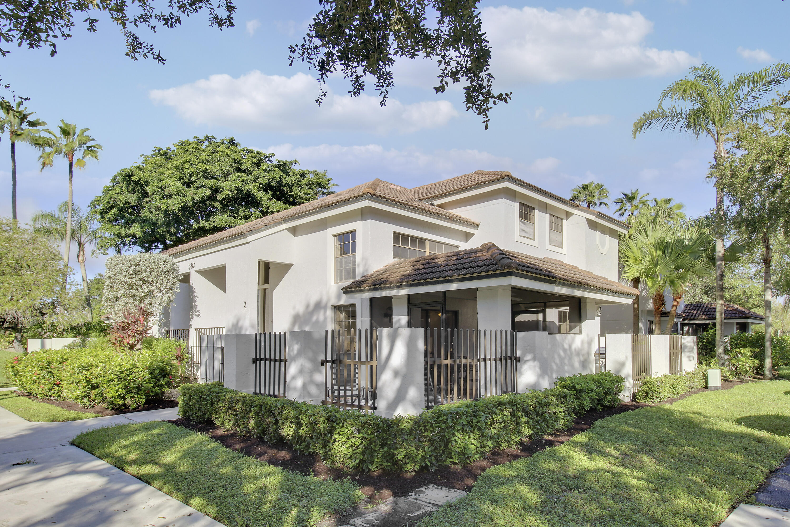 Two-story home with a covered, fenced patio, tan tile roof, and tropical landscaping.