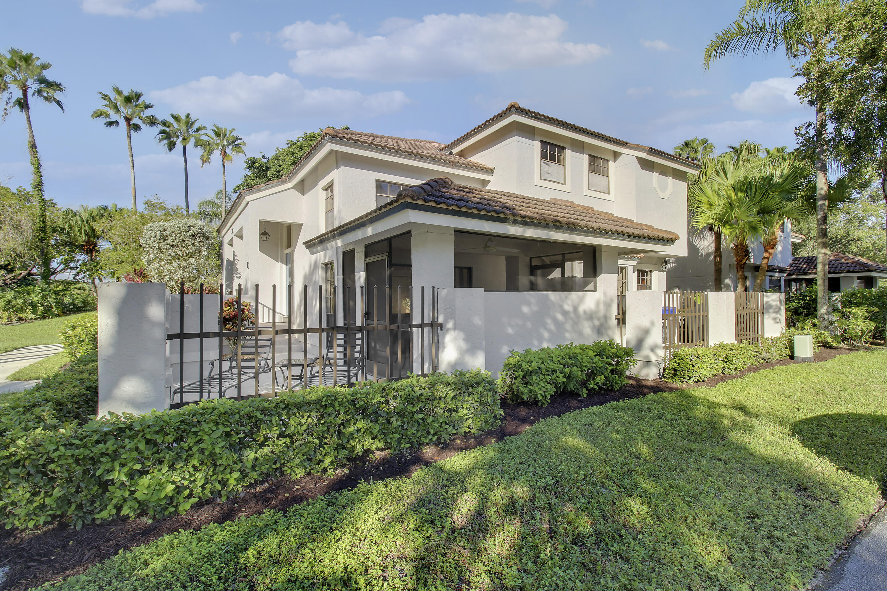 Two-story stucco home with a tiled roof, covered patio, and landscaped yard framed by palm trees.