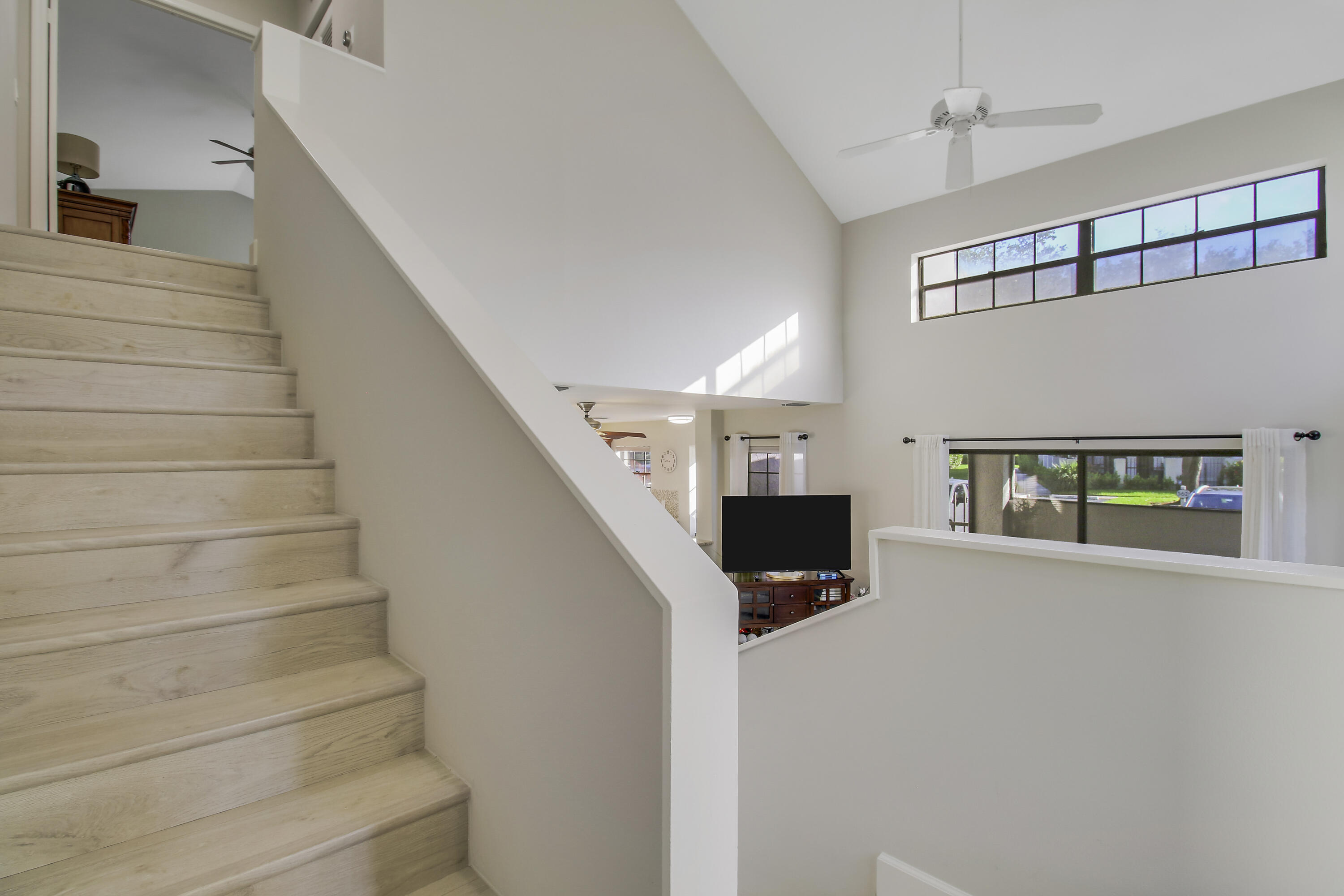 Pale wood staircase rises beside a vaulted ceiling and high windows overlooking the living room.