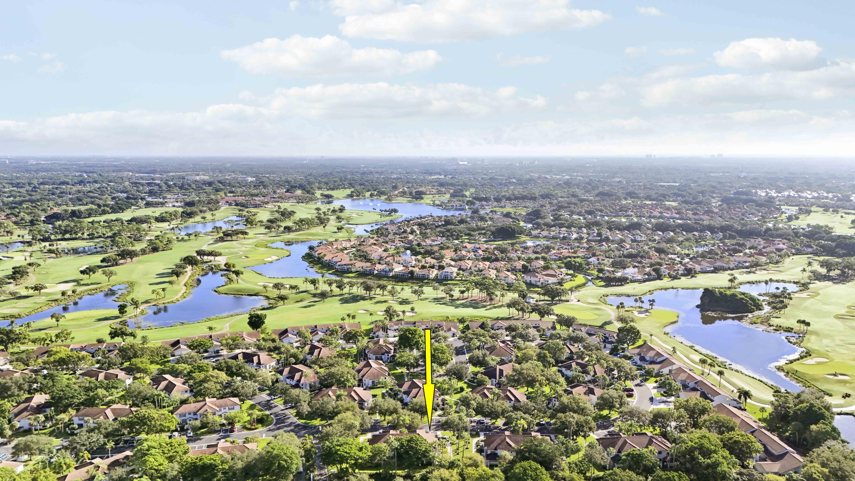 Aerial view of homes beside a golf course and lakes, with a yellow arrow marking the property.