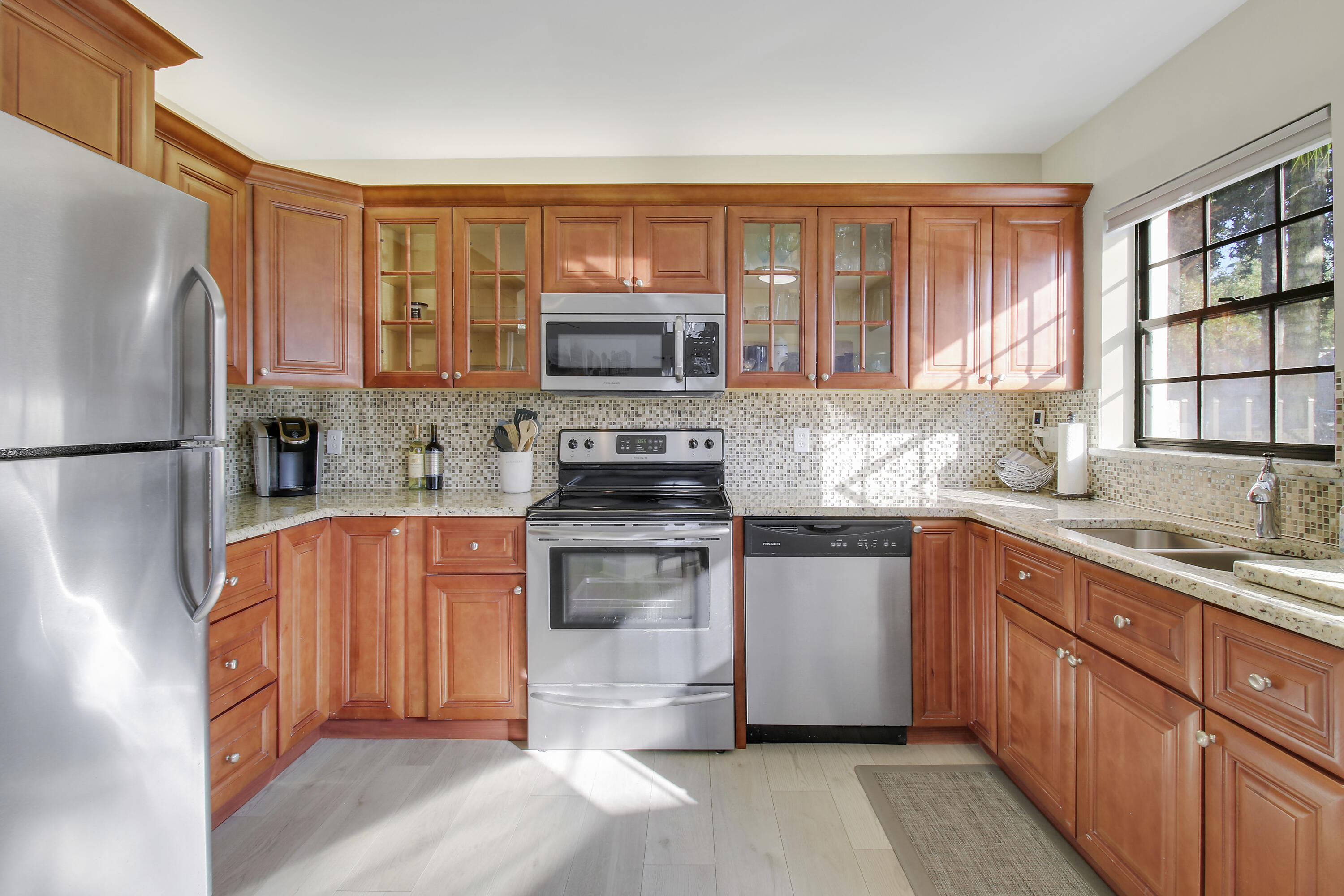 Kitchen with reddish wood cabinetry, stainless steel appliances, and a sunny window above the sink.