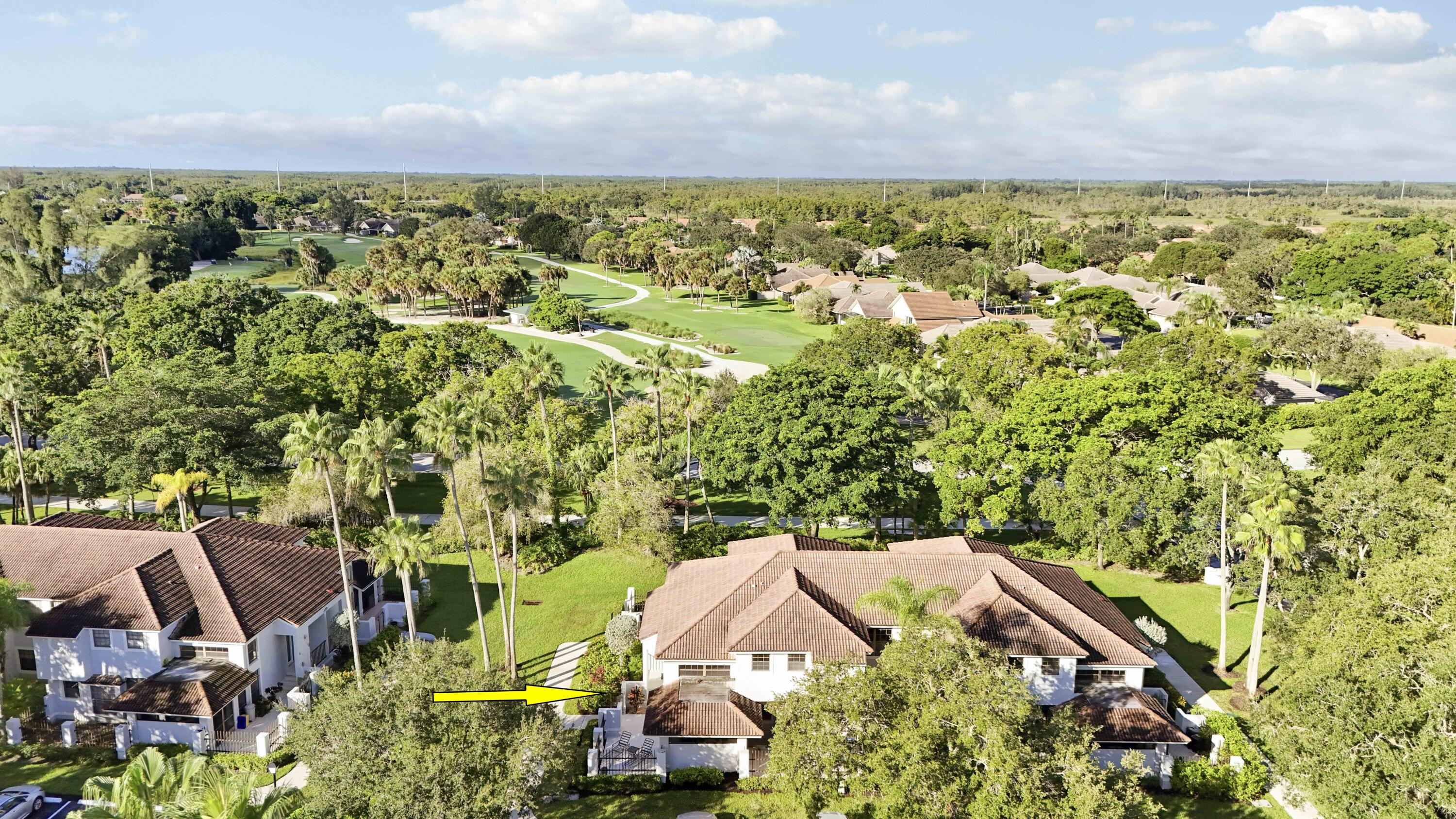 Aerial view of a tiled-roof home beside a golf course, marked by a yellow arrow.