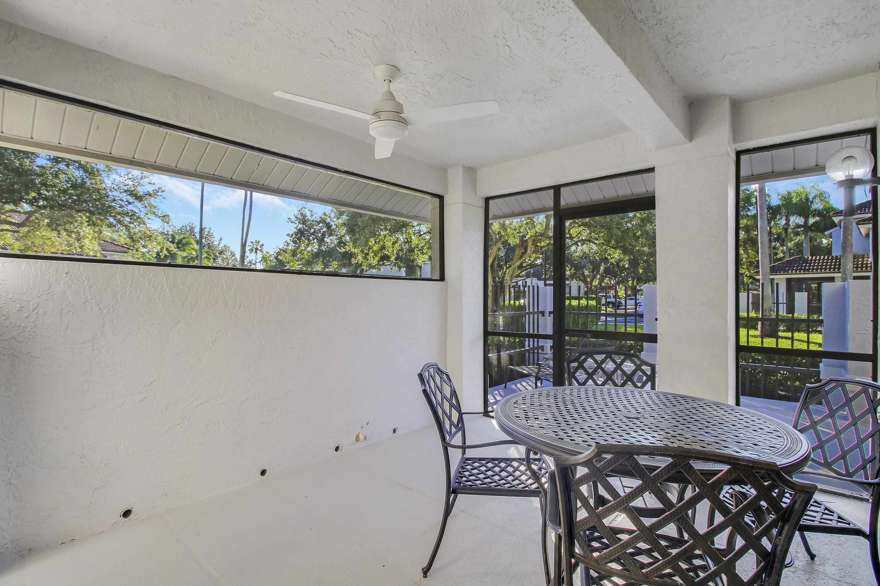 Covered patio with a black metal dining set, ceiling fan, and screened views of leafy trees.