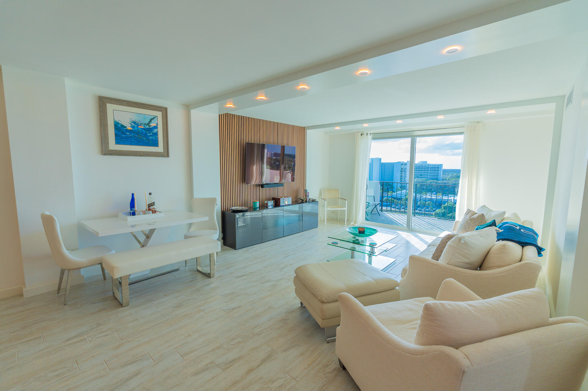 Furnished condo living room with a wood-slat TV wall and balcony doors overlooking nearby buildings.