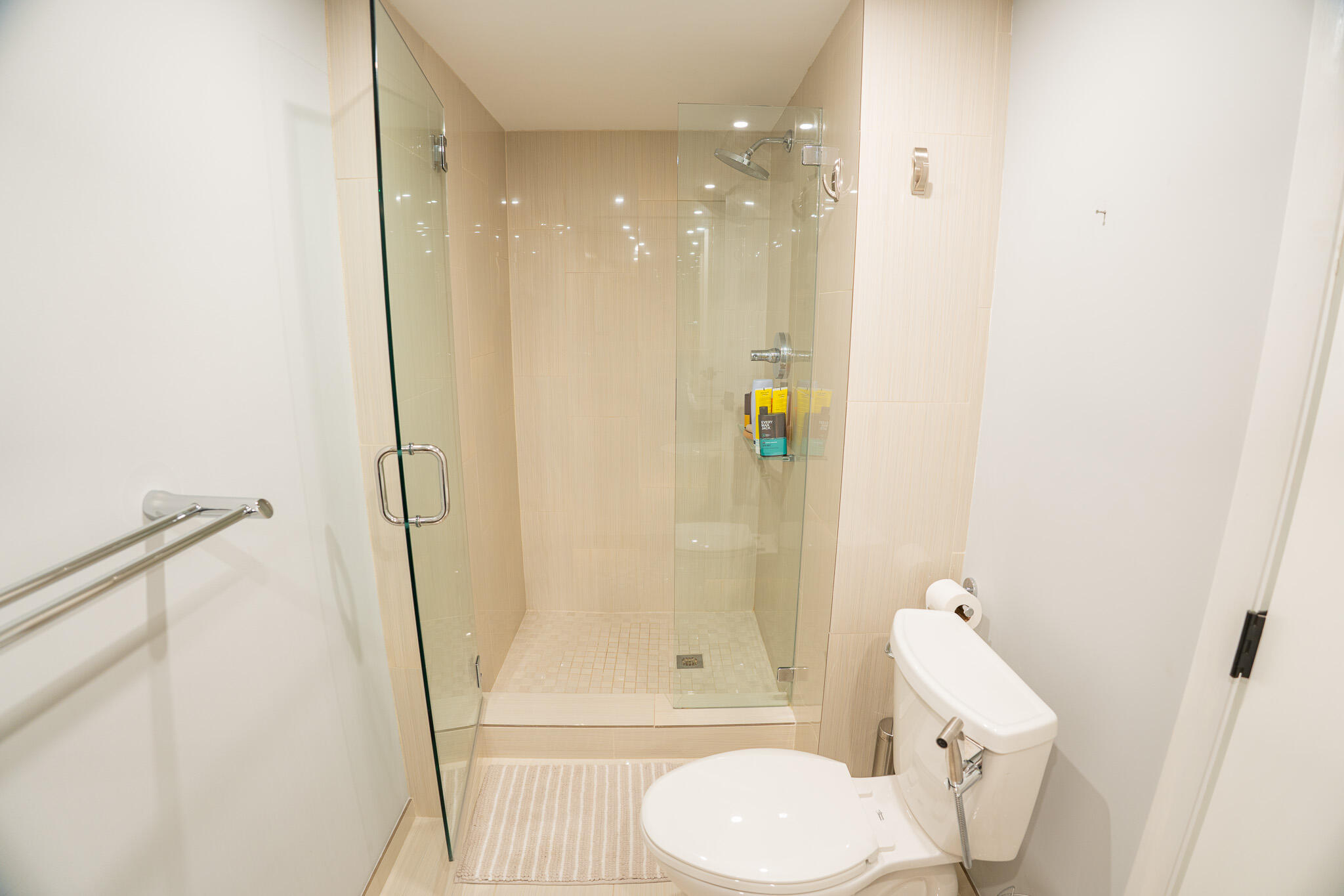 Bathroom with a glass walk-in shower, beige tile, and a white toilet.