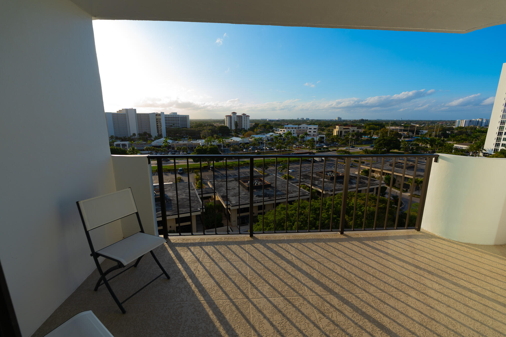 Condo balcony with a folding chair and an expansive view of nearby buildings and greenery.