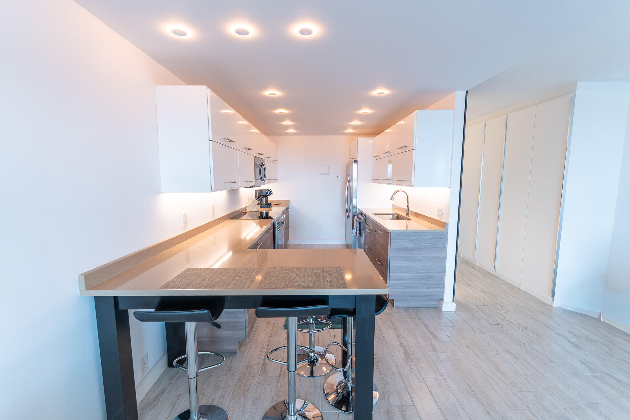 Modern galley kitchen with white cabinets, stainless appliances, and a breakfast bar with stools.