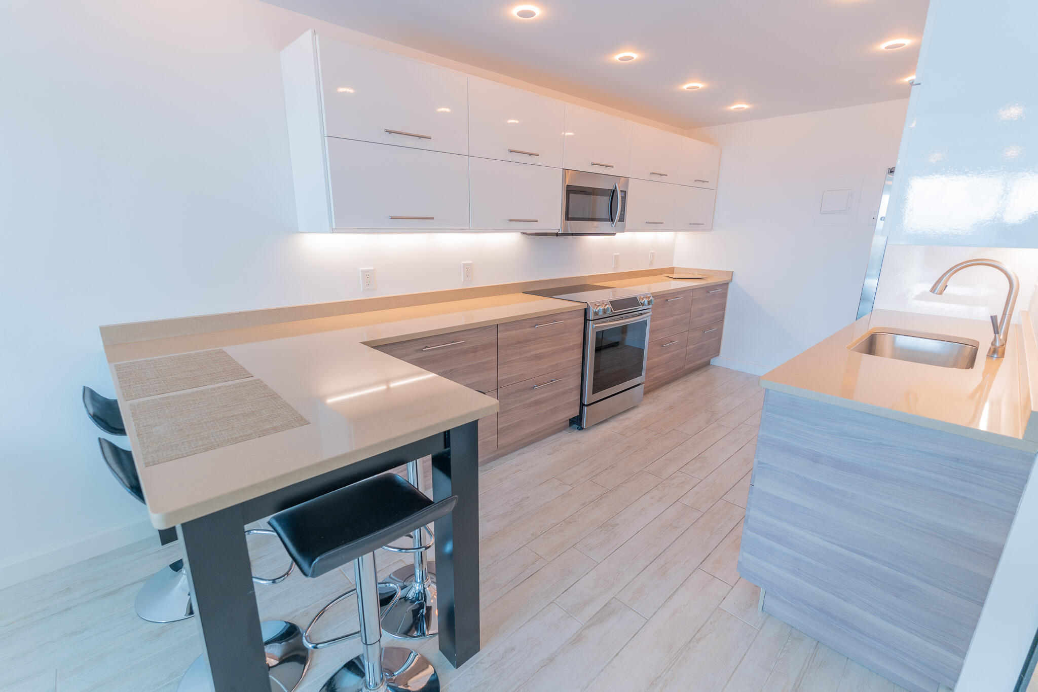 Modern kitchen with pale stone counters, wood-tone cabinets, stainless appliances, and a bar-stool peninsula.