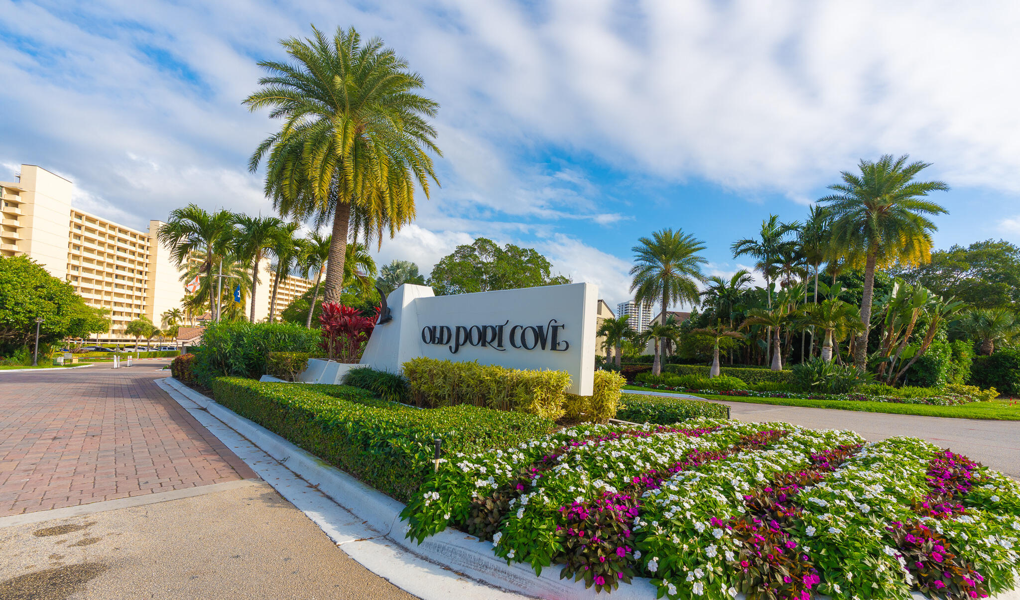 Old Port Cove entrance sign amid palm trees and colorful flower beds.