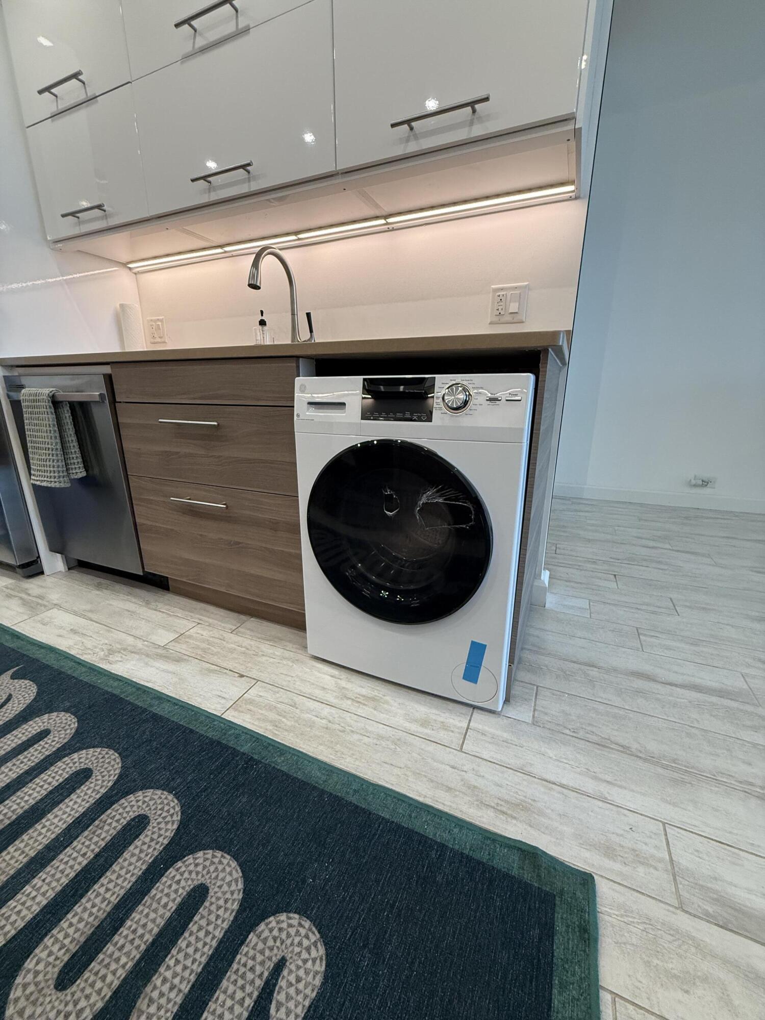 Laundry area with a front-loading washer, wood drawers, white cabinets, and a sink.