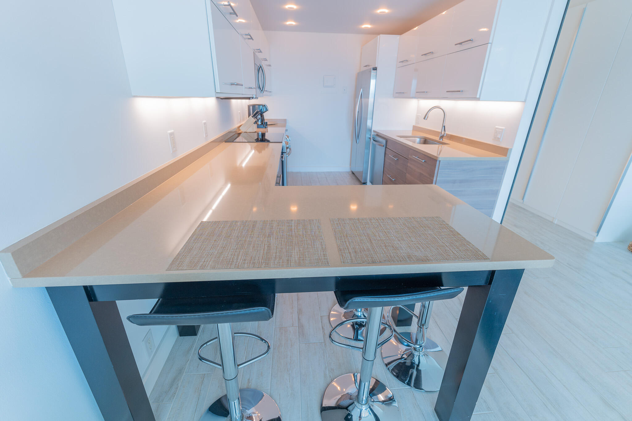 Modern kitchen with white cabinets, stainless appliances, and a breakfast bar with chrome stools.