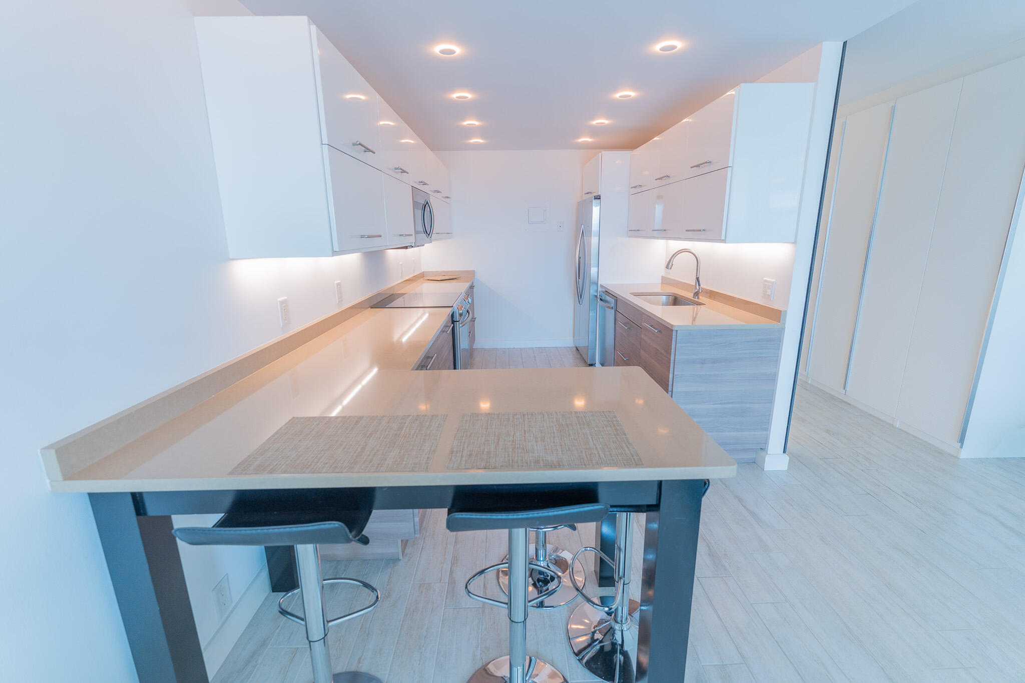 Modern galley kitchen with white cabinets, stainless appliances, and a large breakfast bar with stools.