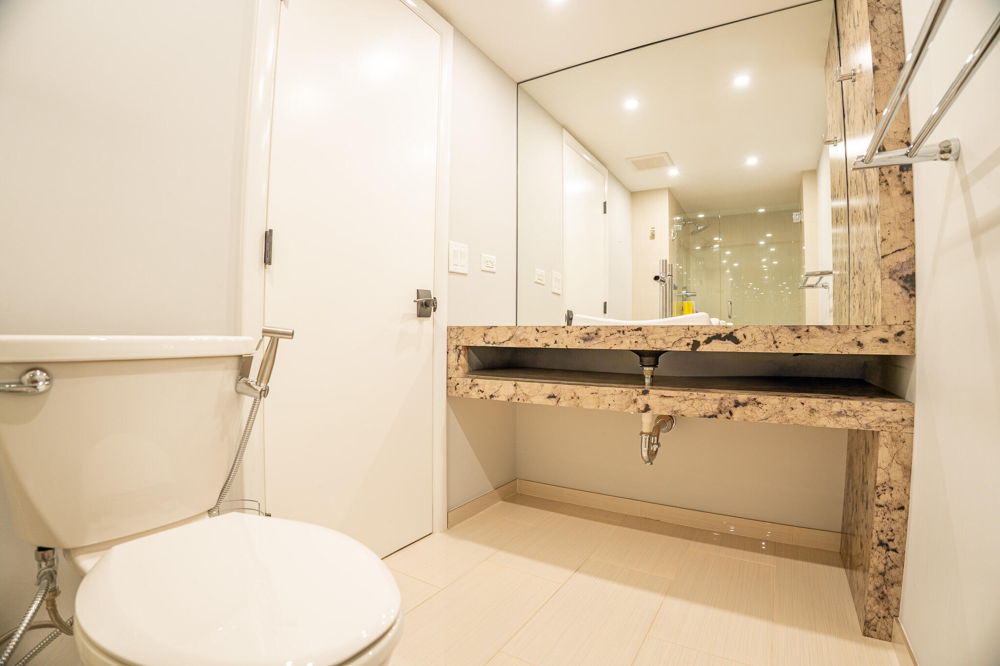 Modern bathroom with a mottled stone vanity, large mirror, and glass-enclosed shower.